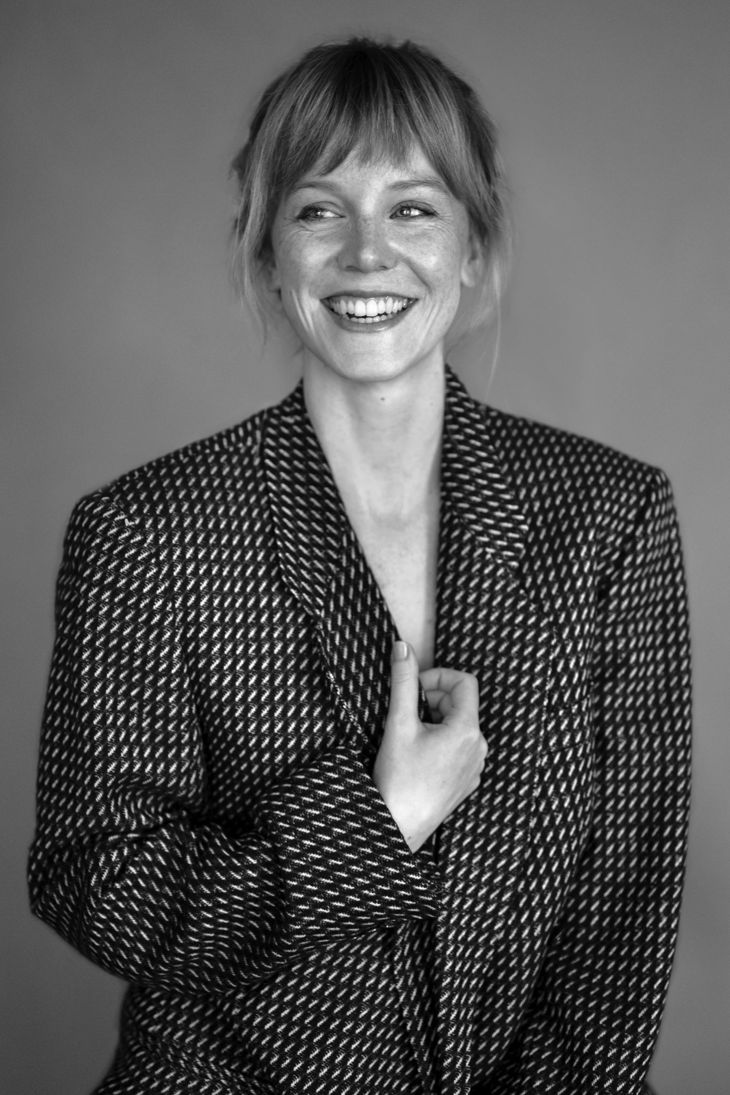 A woman with short hair, smiling and wearing a patterned blazer, looking to her right.