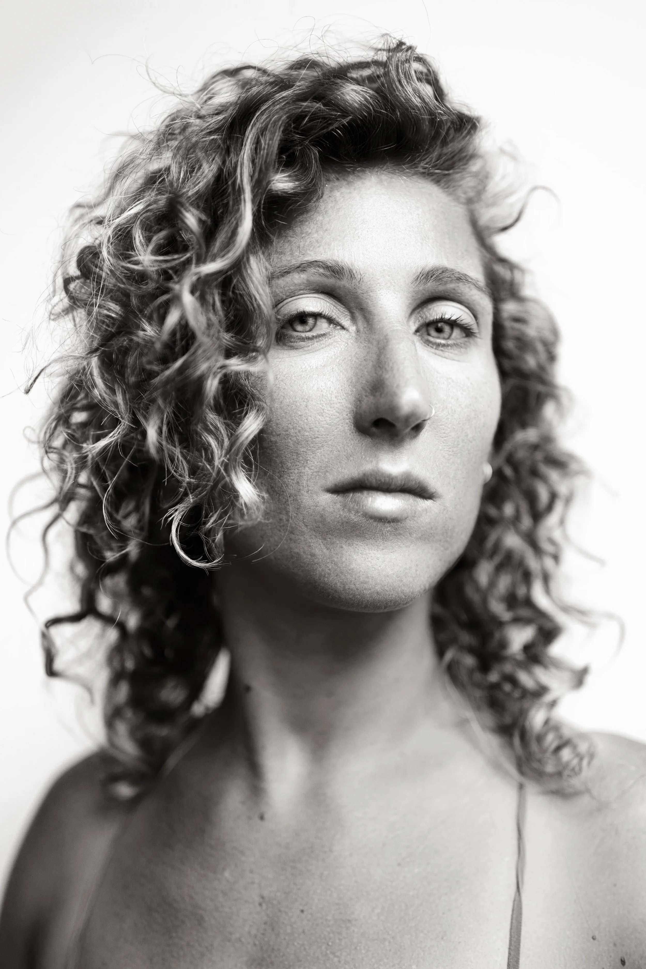 A black-and-white close-up portrait of a woman with curly hair, freckles, and a serious expression.