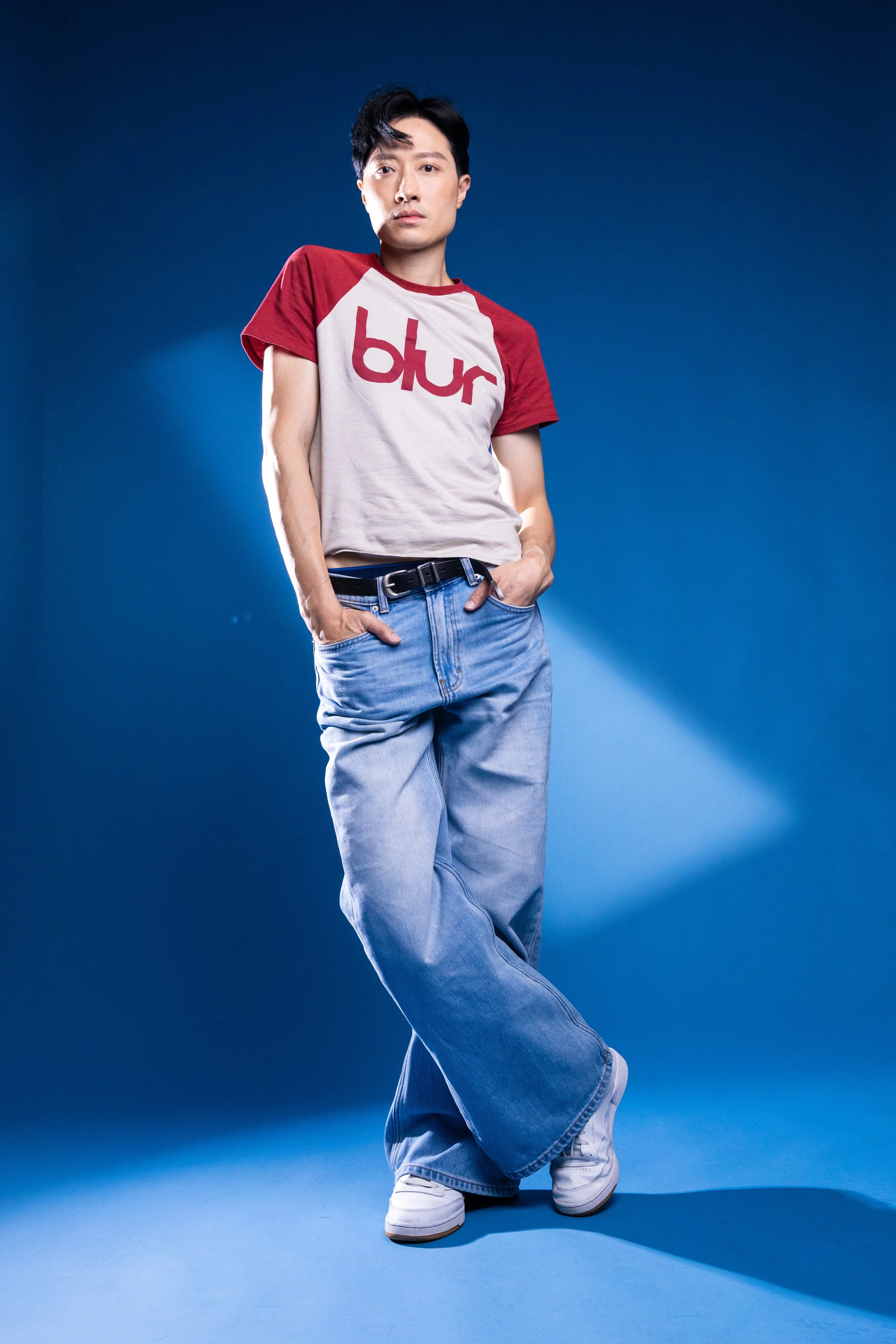 Young man in a Beats t-shirt and baggy jeans standing against a blue background.