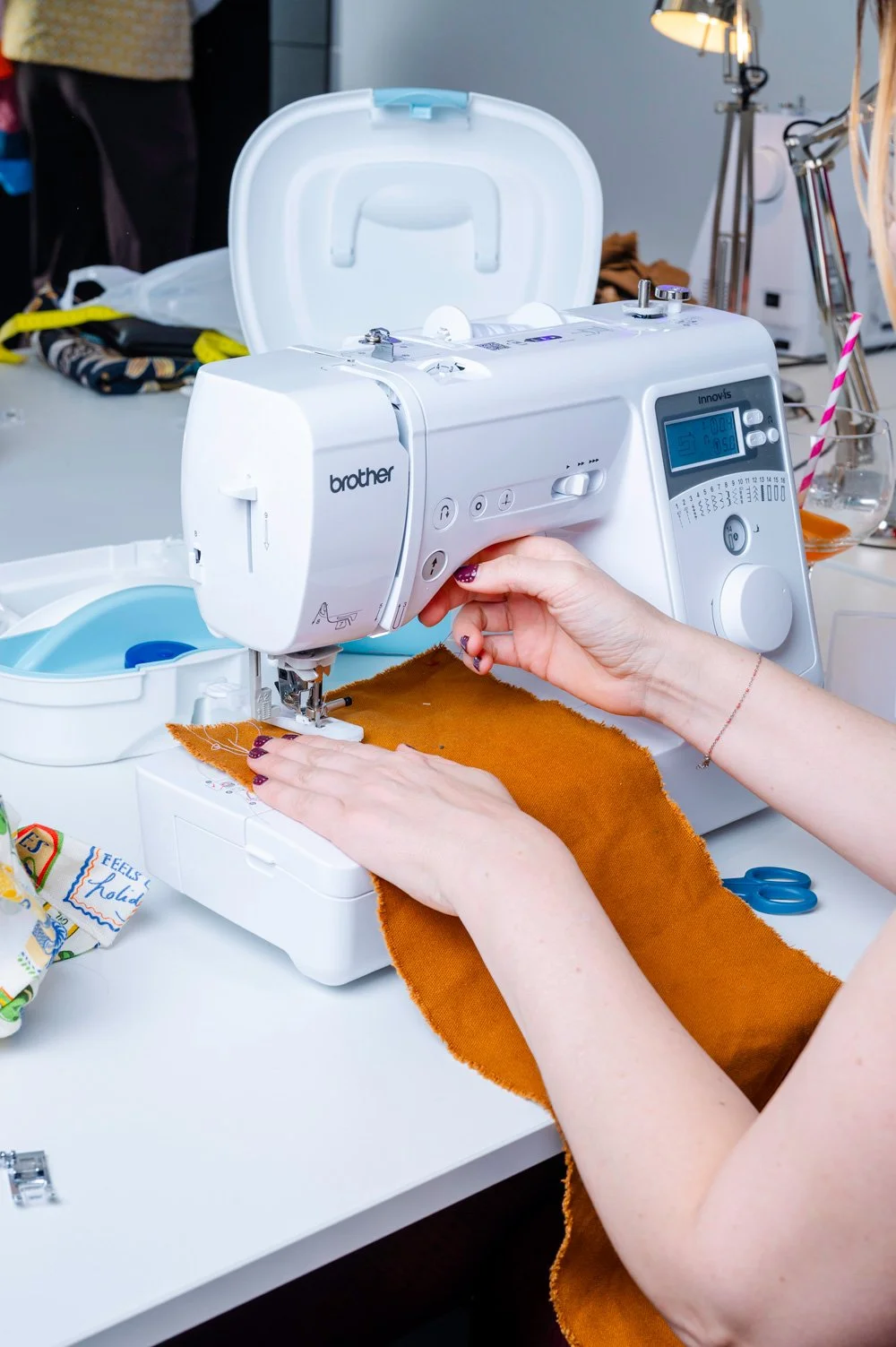Close-up of a person sewing orange fabric with a white Brother sewing machine in a well-lit workspace.