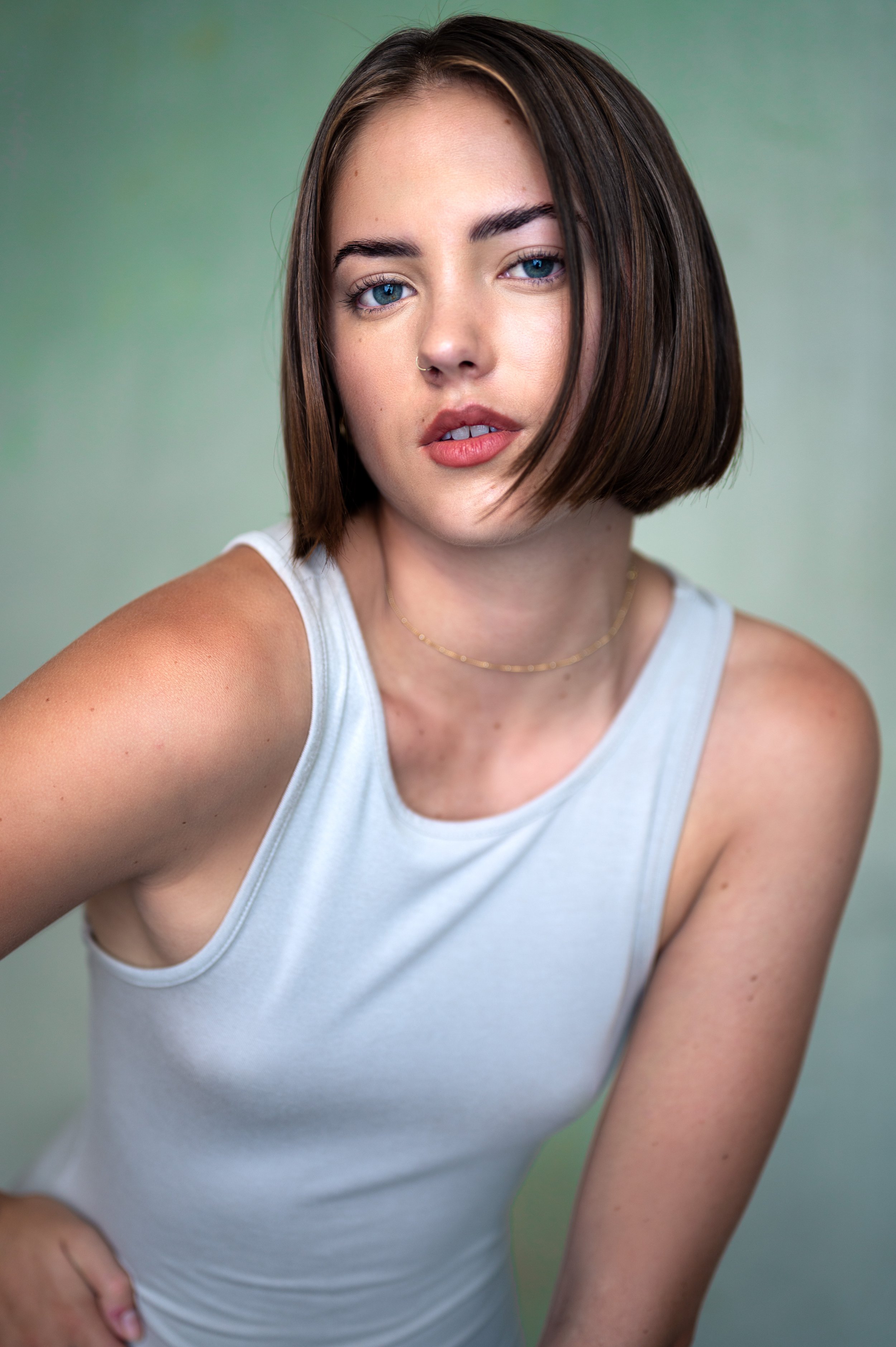 A young woman with shoulder-length brown hair and blue eyes posing against a green background.