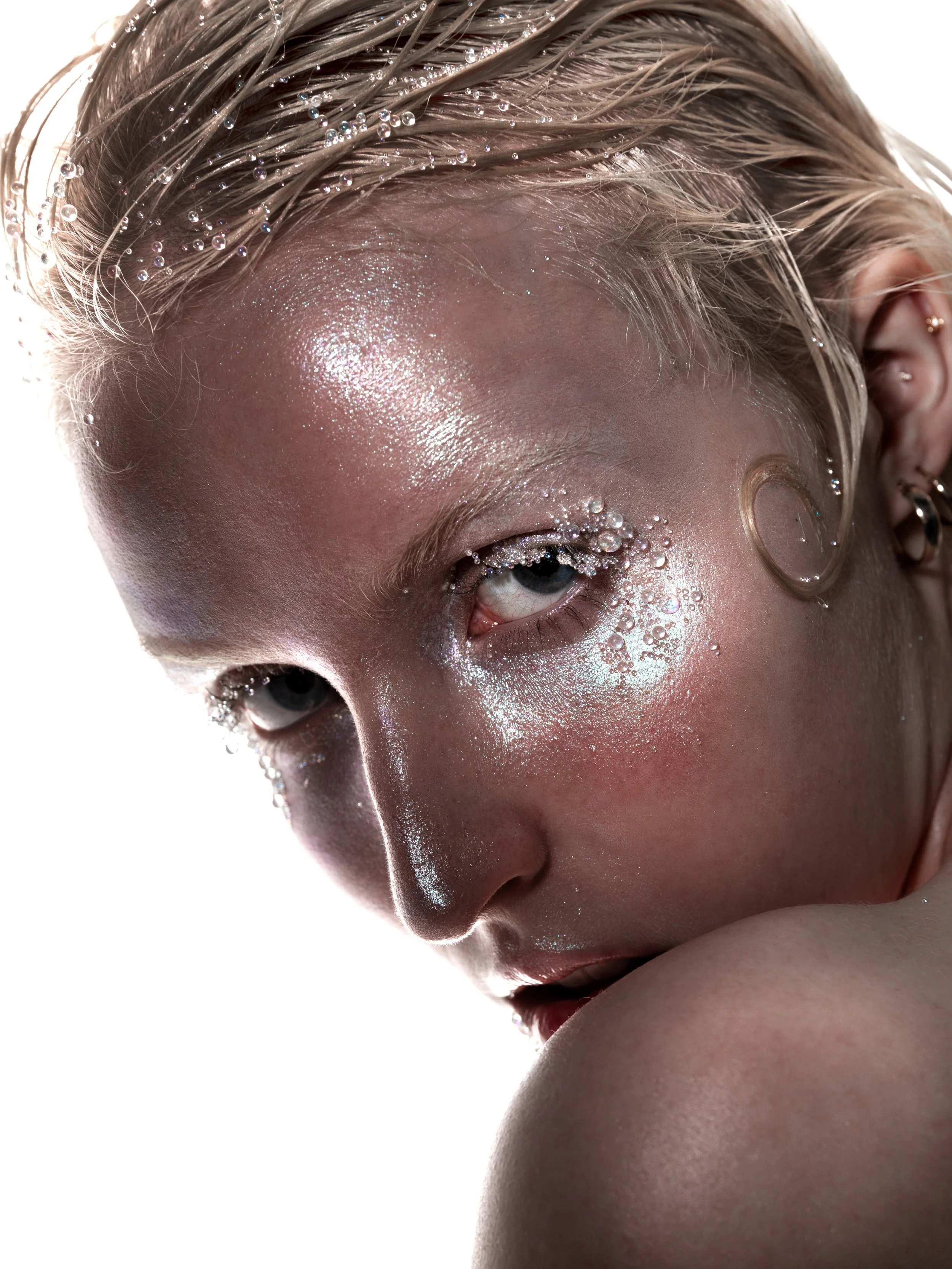 Close-up of a person with wet, glittery makeup and small water bubbles on their face and hair.