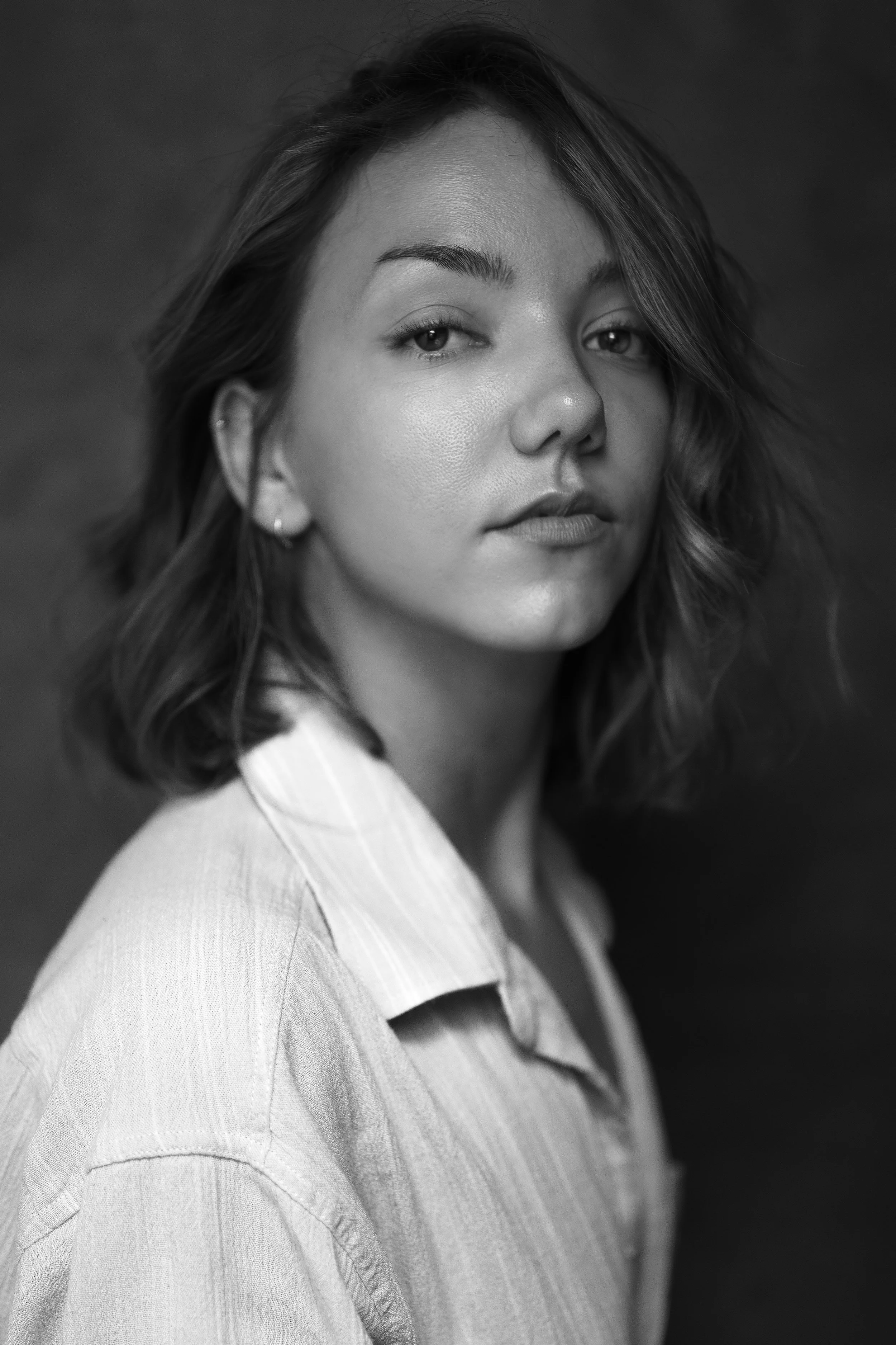 A black and white portrait of a young woman with shoulder-length wavy hair, wearing a collared shirt, looking slightly to the side with a neutral expression.