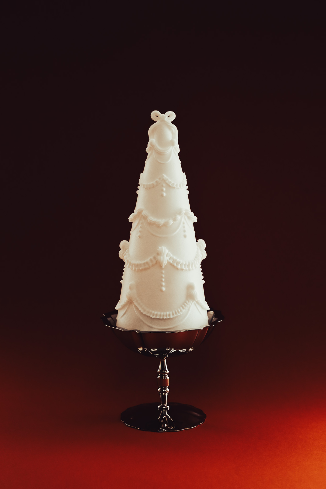A white conical Christmas cake shaped like a Christmas tree, decorated with icing garlands and ornaments, displayed on a dark glass cake stand against a dark background.