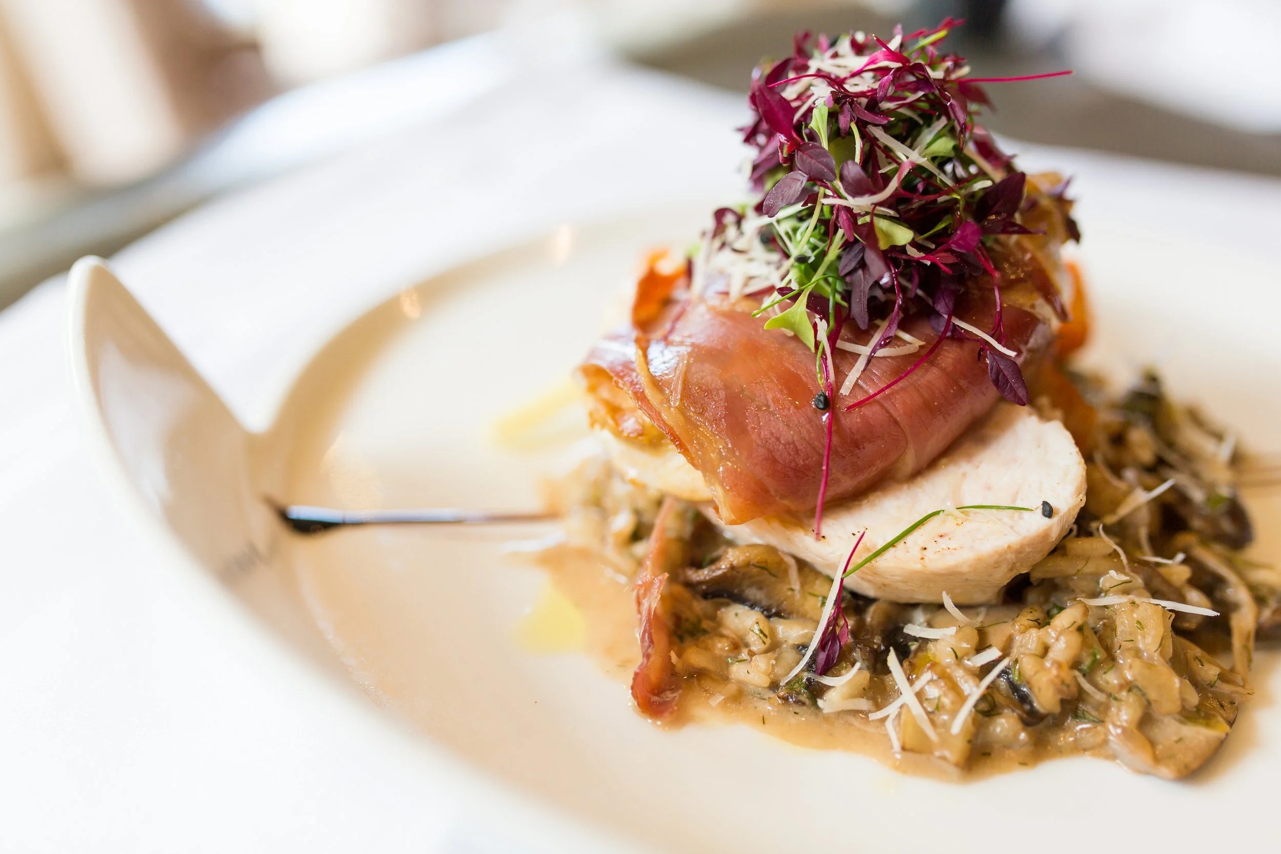 Gourmet dish with sliced meat, microgreens, and a creamy mushroom risotto on a white plate.