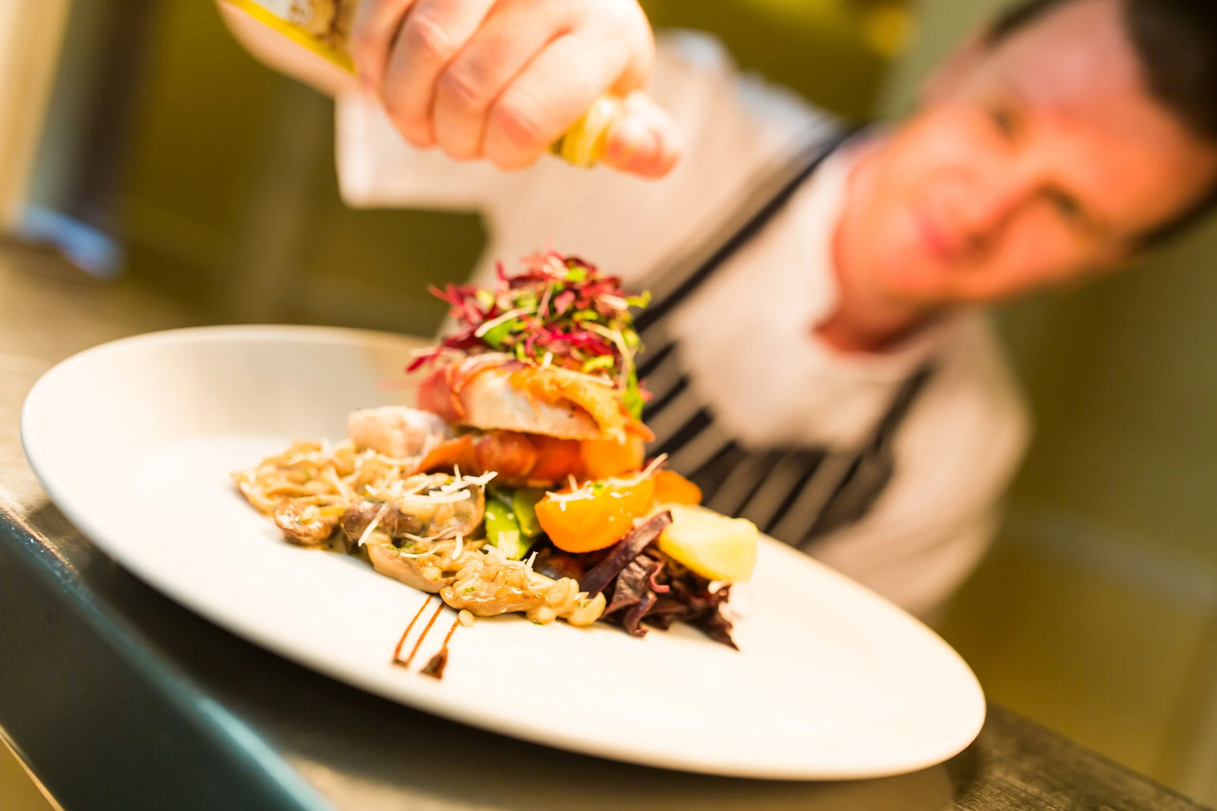 Chef garnishing a gourmet dish with microgreens on a white plate.