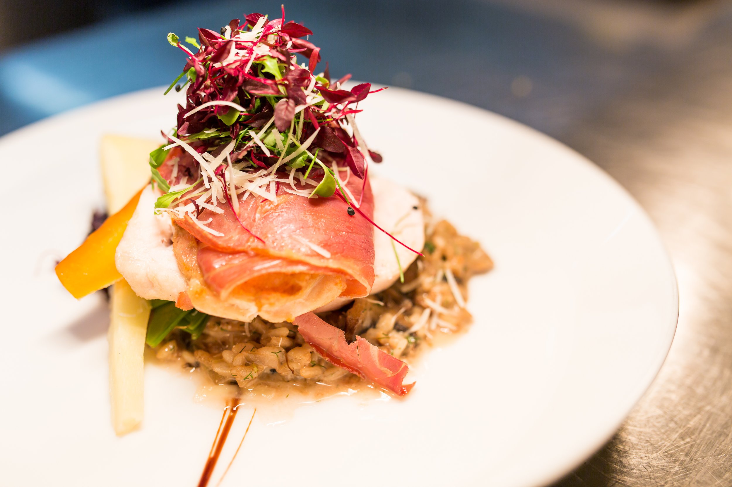 A plated gourmet dish with microgreens, cured meat, rice, and vegetables on a white plate.