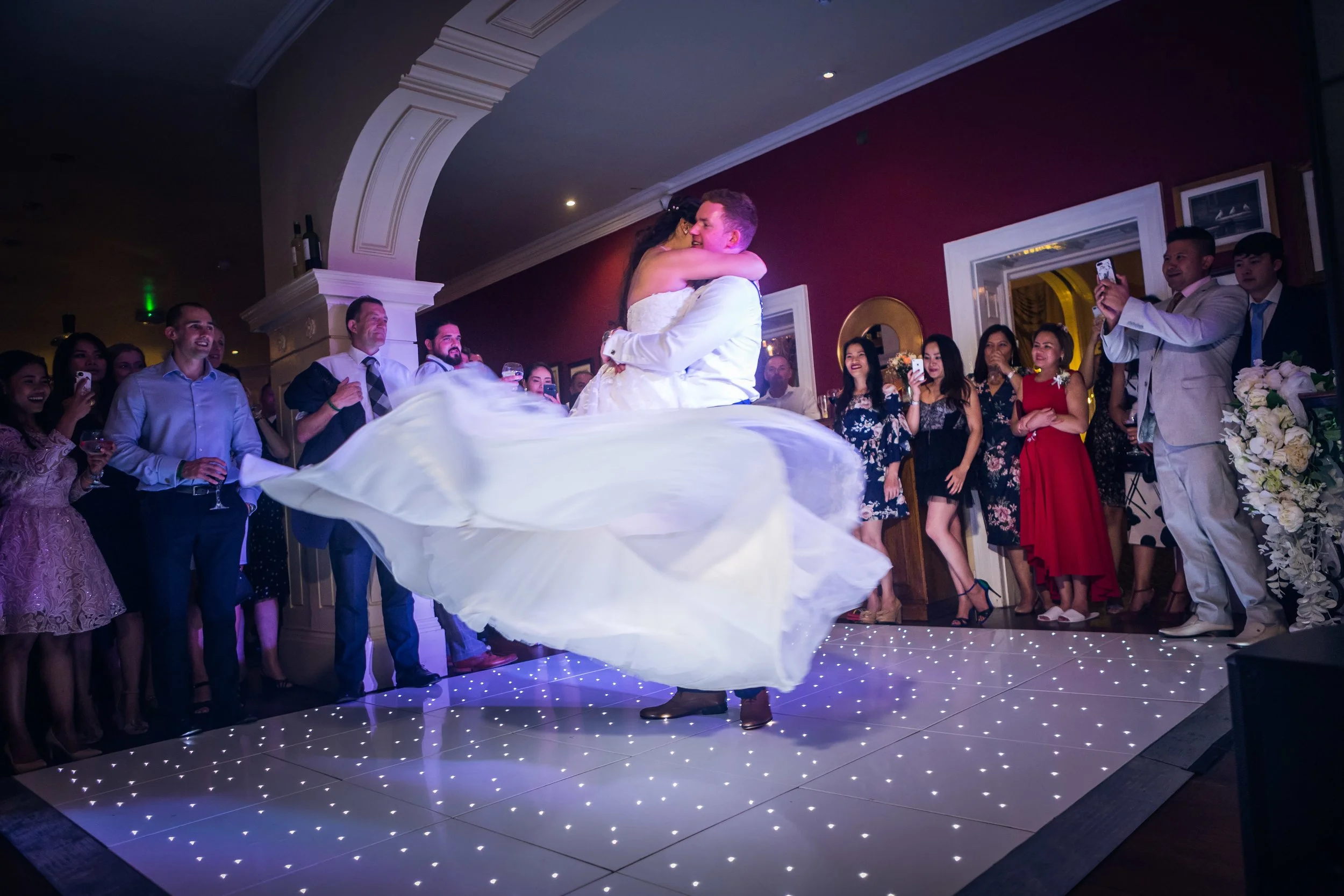 Bride and groom dancing at their wedding reception surrounded by guests taking photos and watching