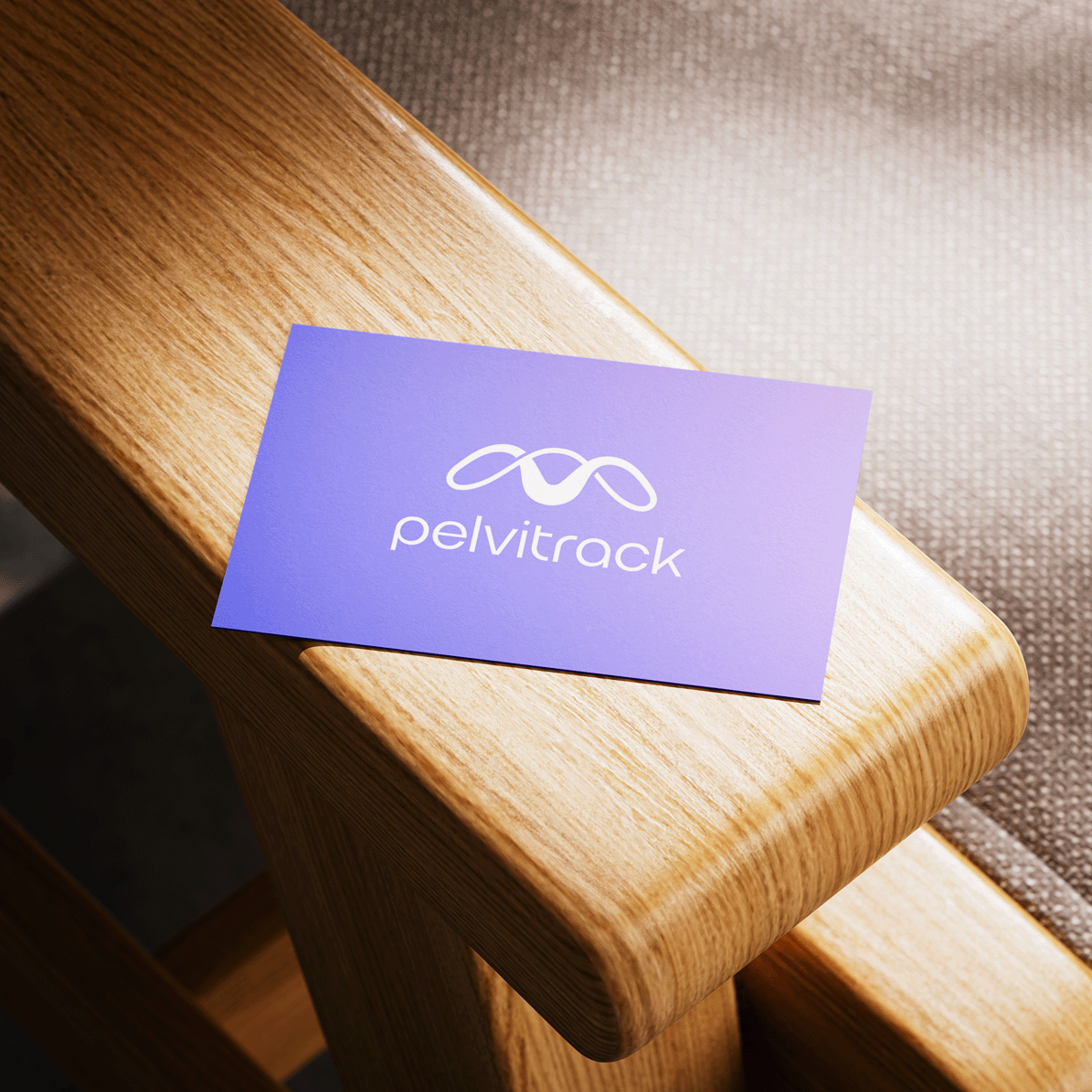 Purple business card with white logo and text that reads "pelvitrack" placed on a wooden surface next to a fabric surface.