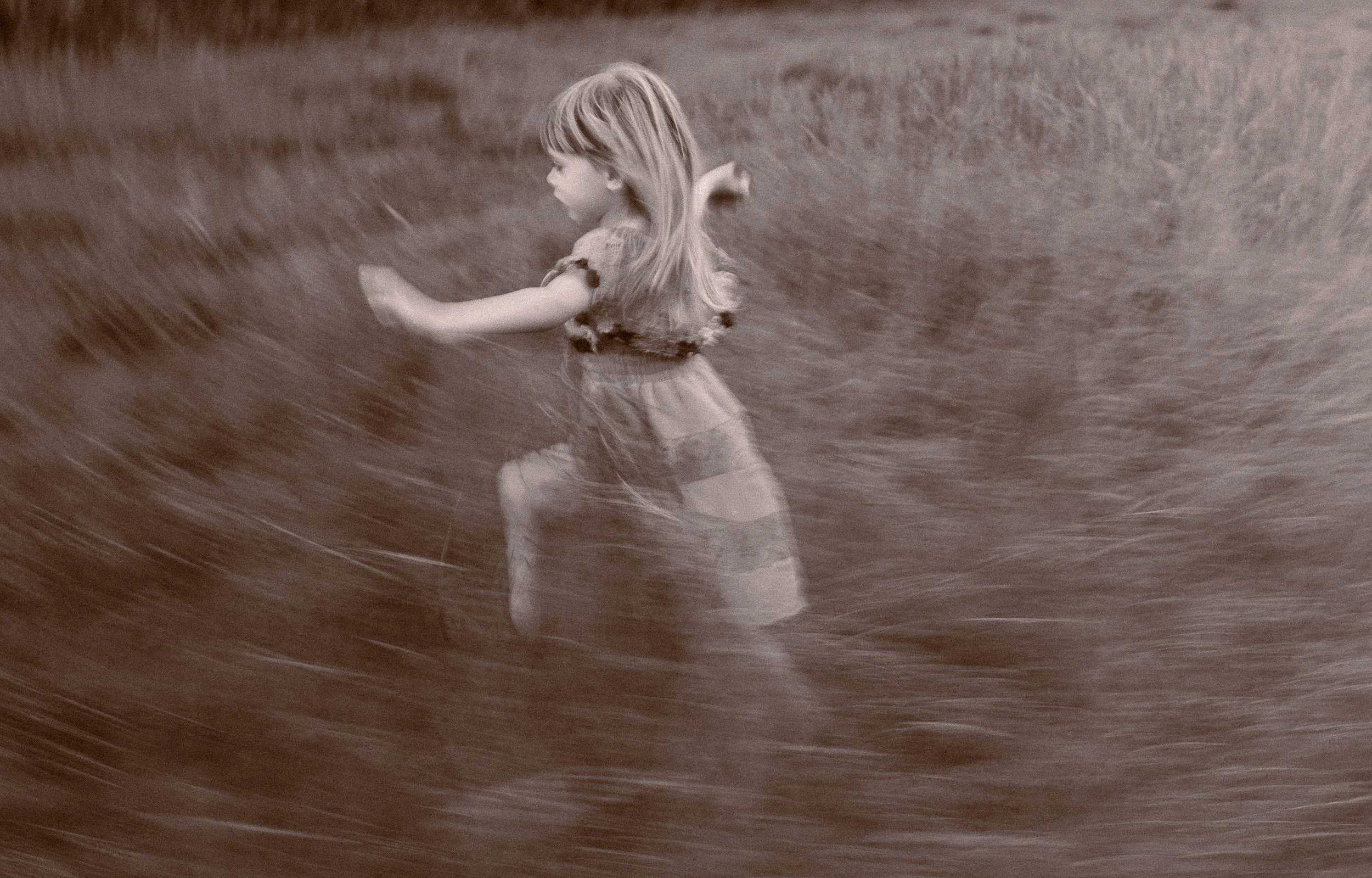 A young girl races through the  in long grass during a relaxed outdoor family photography session in Amersham, Buckinghamshire at sunset