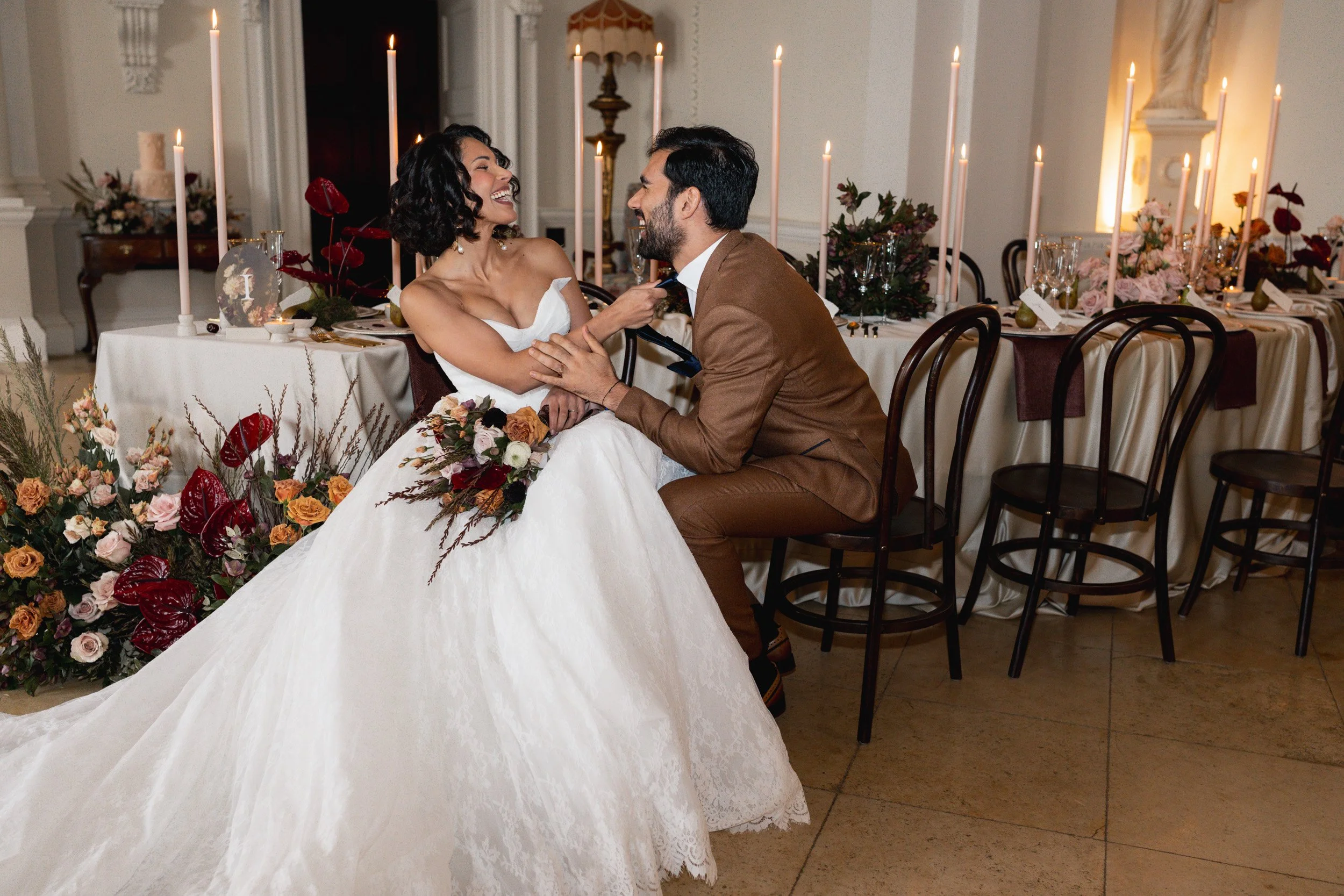 Bride playfully pulling her groom by his tie while laughing  at their candlelit head table at Kirtlington Park in Oxfordshire