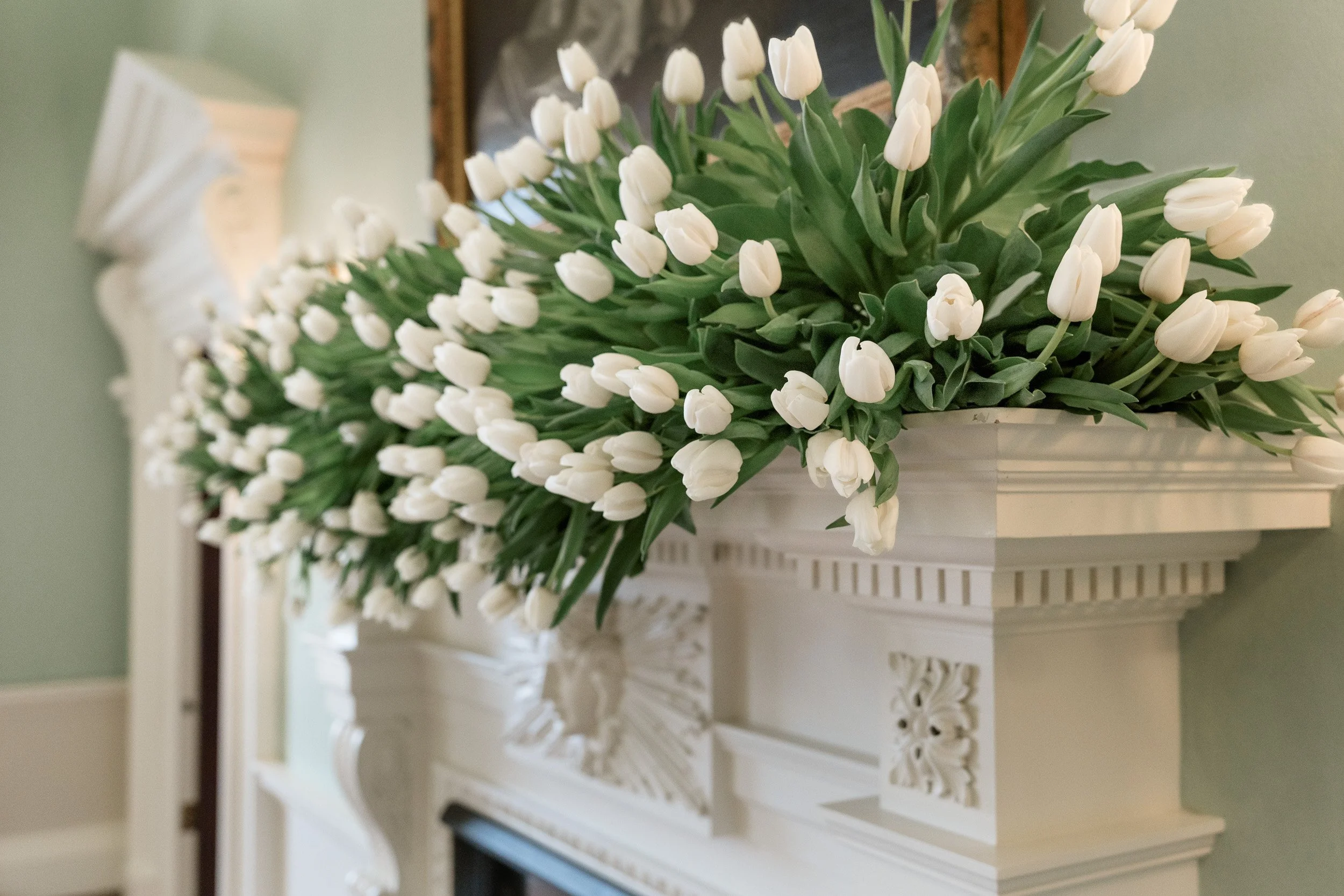 White tulips aisle arranged along the fireplace mantel during the wedding reception at Kirtlington Park in Oxfordshire