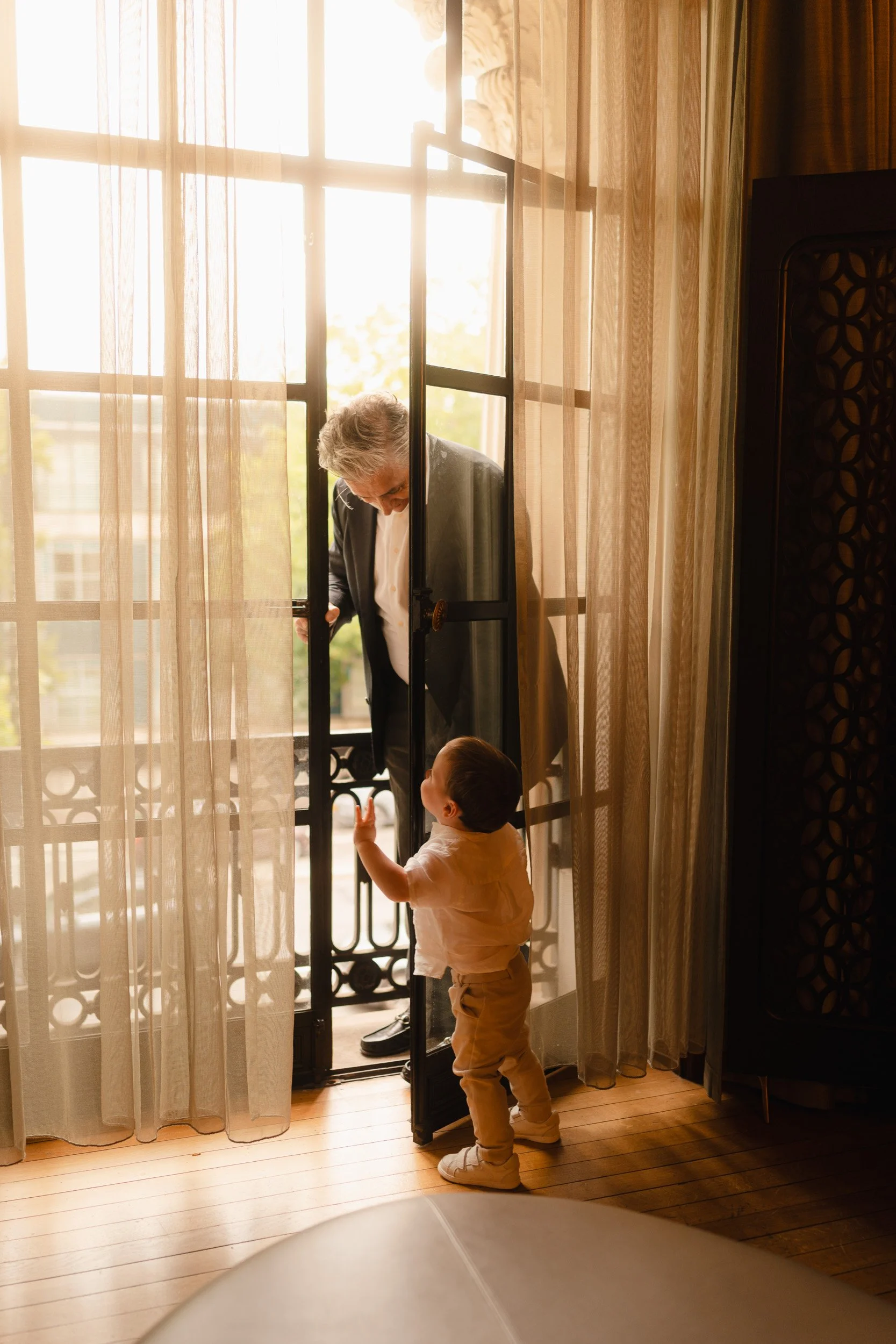 Father of the bride gazes down at his grandson in  golden window light  at Marylebone Town Hall Registry Office in London 