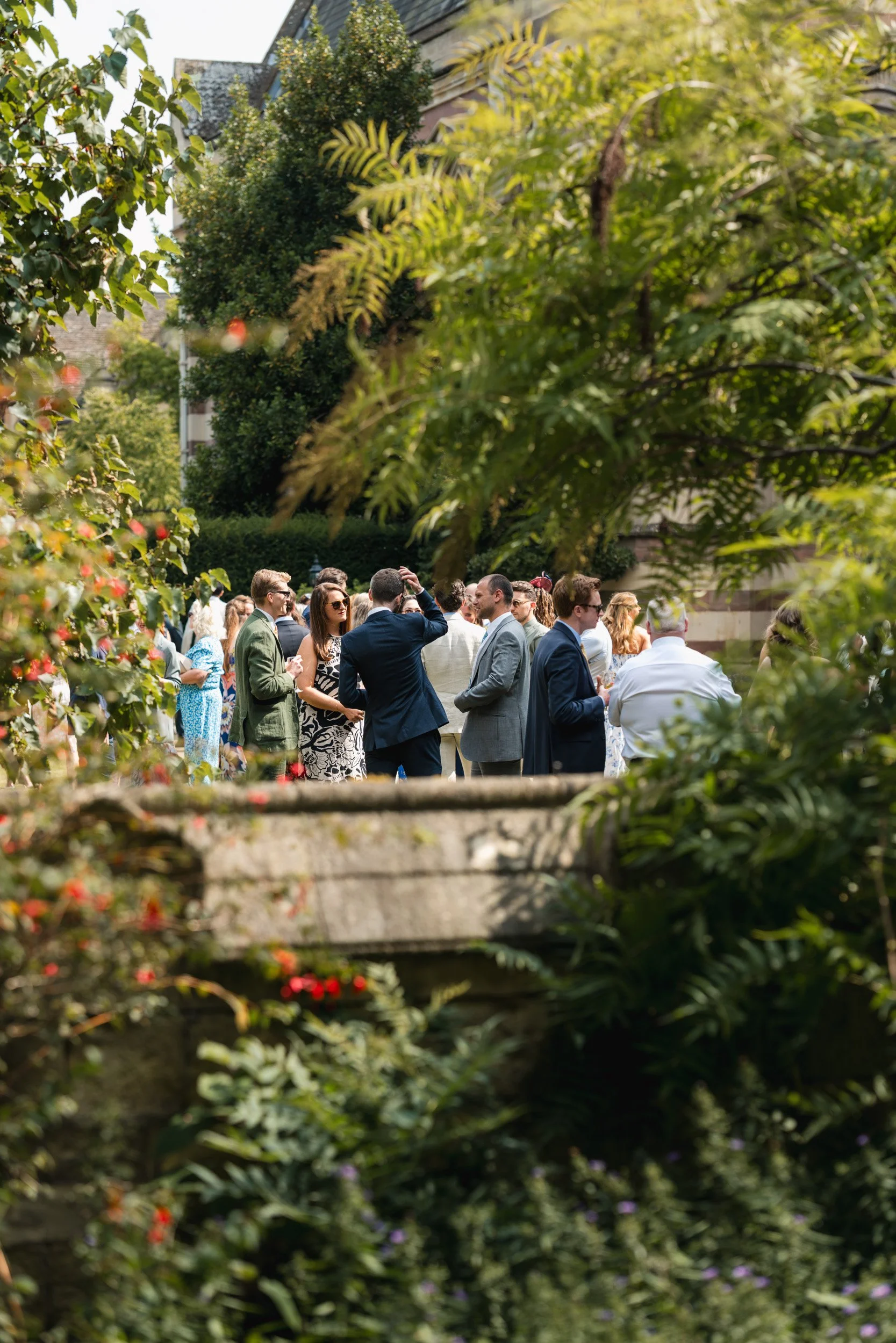 Wedding guests enjoying outdoor drinks in  the historic gardens of an Oxford University college after the wedding ceremony in Oxford, England