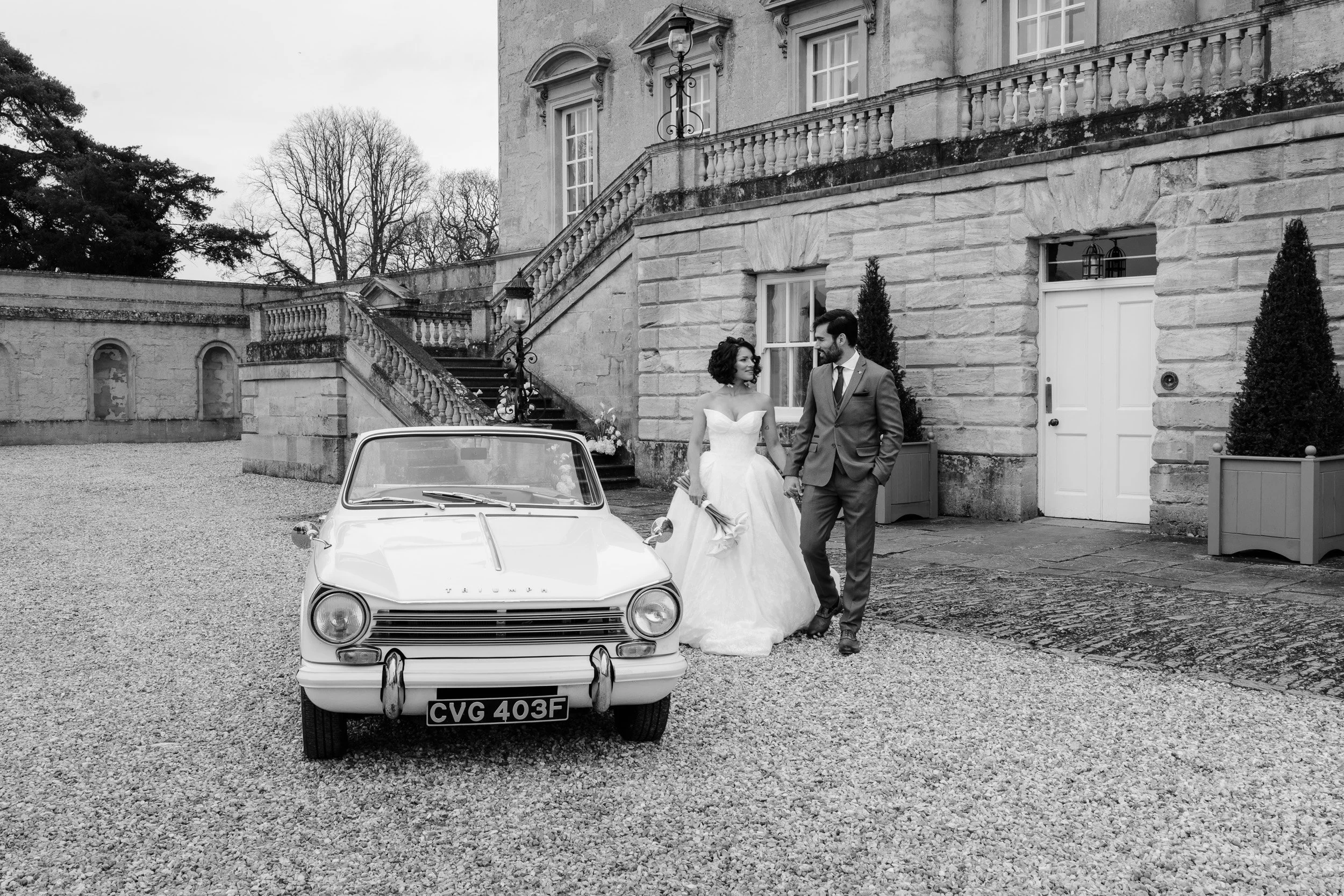 Bride and groom walking towards a Vintage  car outside Kirtlington Park in Oxfordshire