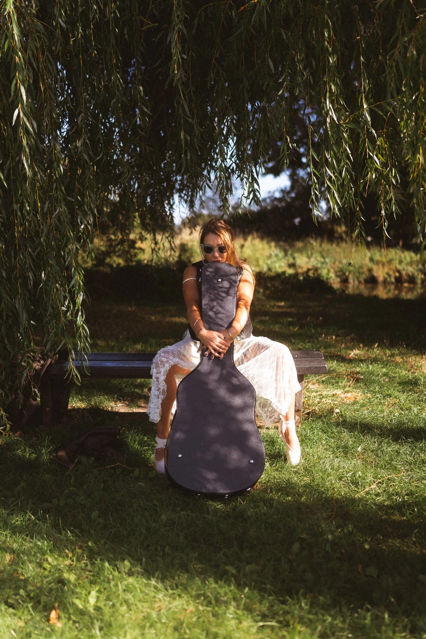 Musician and dancer sitting under a willow tree in a park in Windsor Berkshire with her guitar on a brand shoot