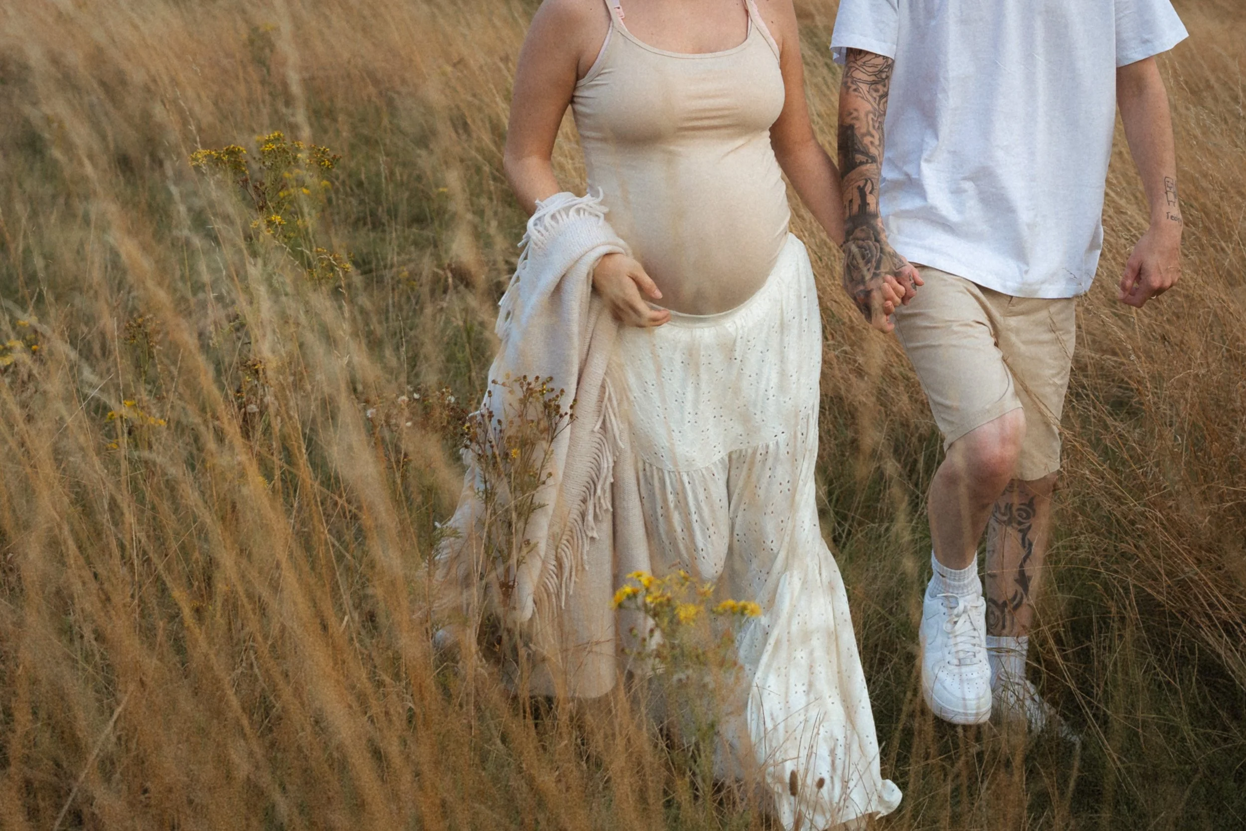 Close up of husband holding his pregnant wife's hand walking though  the log grasses of a meadow in Great Missenden, Buckinghamshire