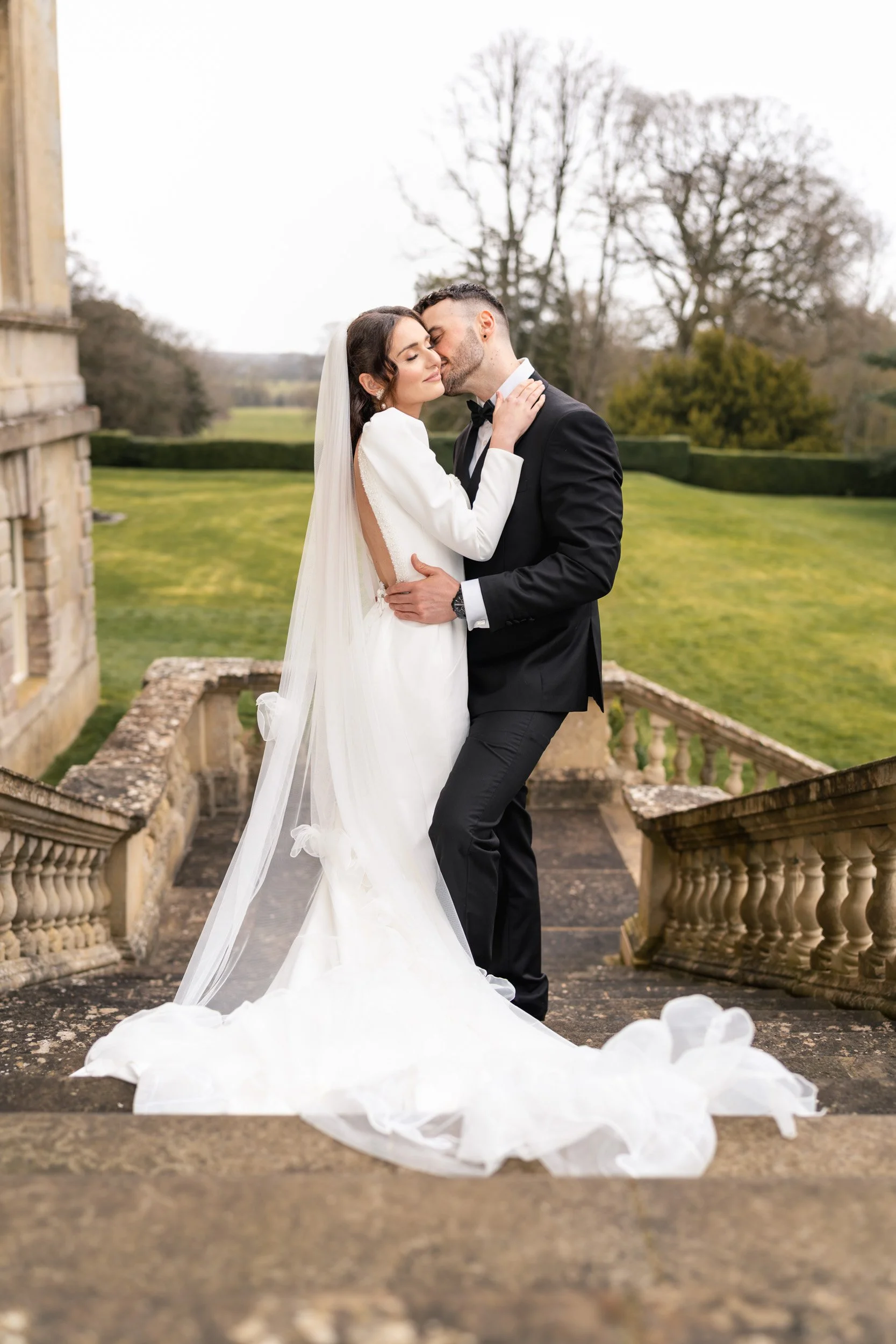 Groom kissing the brides neck on the garden steps at Kirtlington Park in Oxfordshire