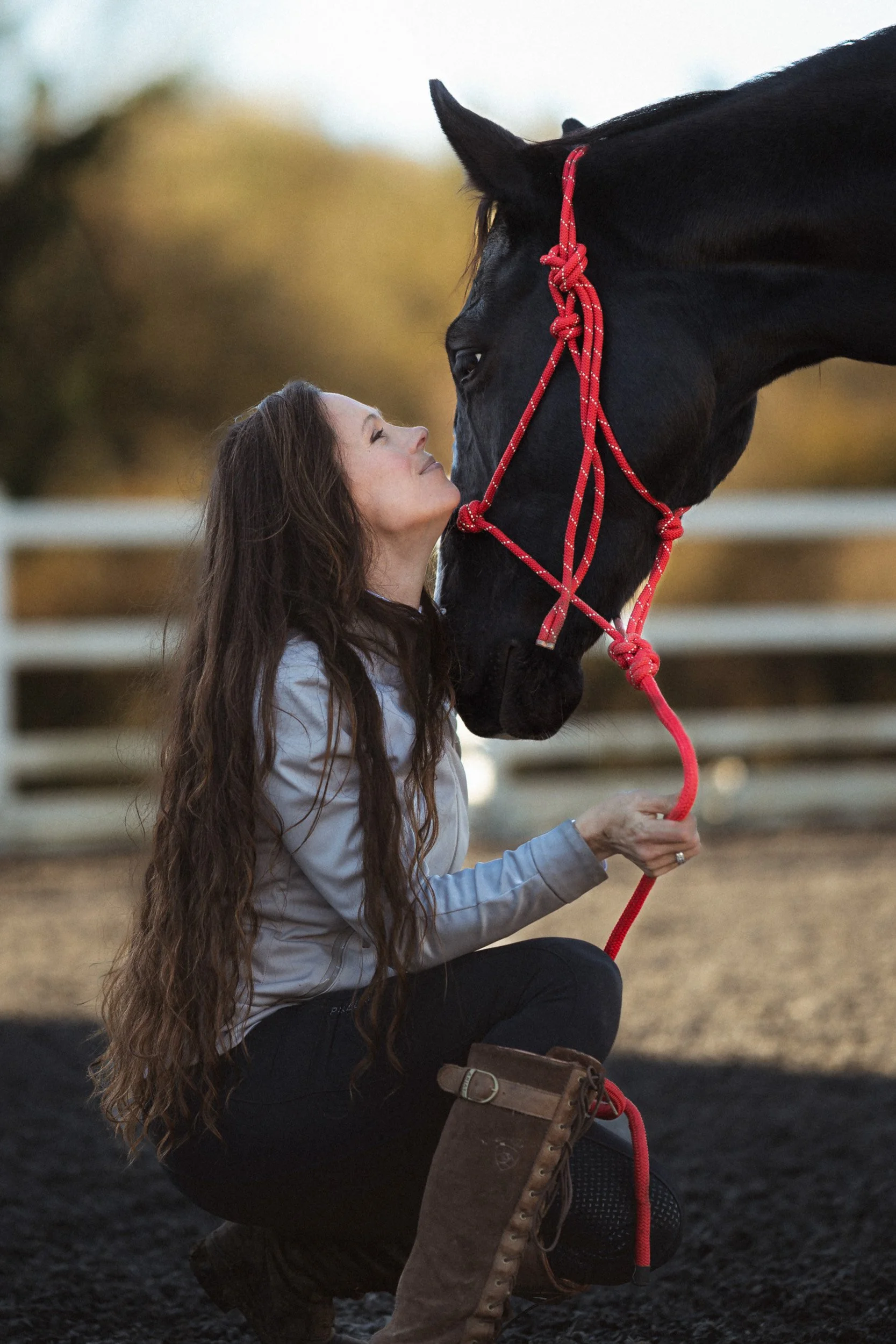 Equestrian fitness coach kneeling beside her horse in the arena  at Sean Hardy Horse Training in Great Missenden Buckinghamshire during a branding photoshoot