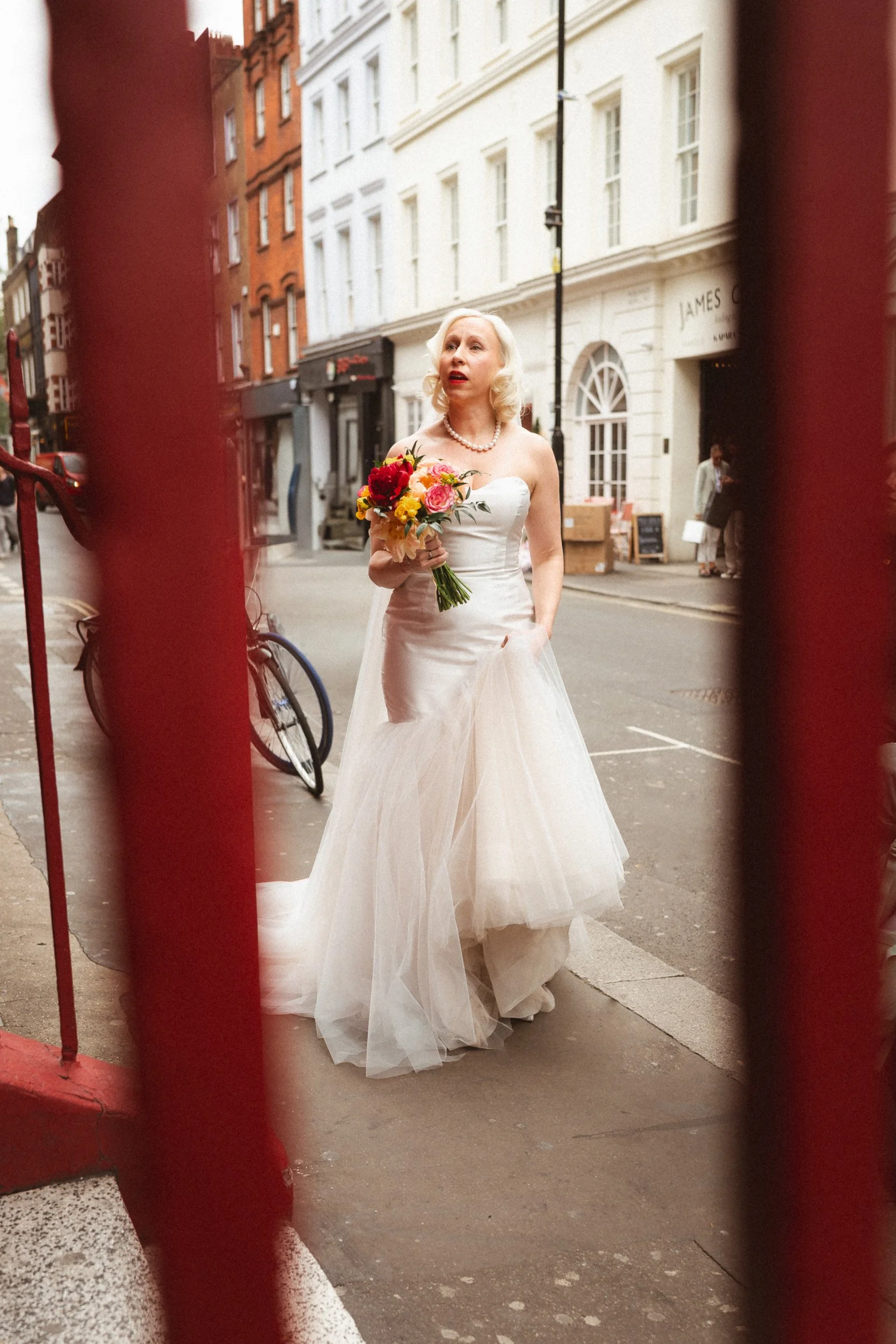 Bride looking for her bridesmaids outside The Union Club in Soho, photographed through the handrails