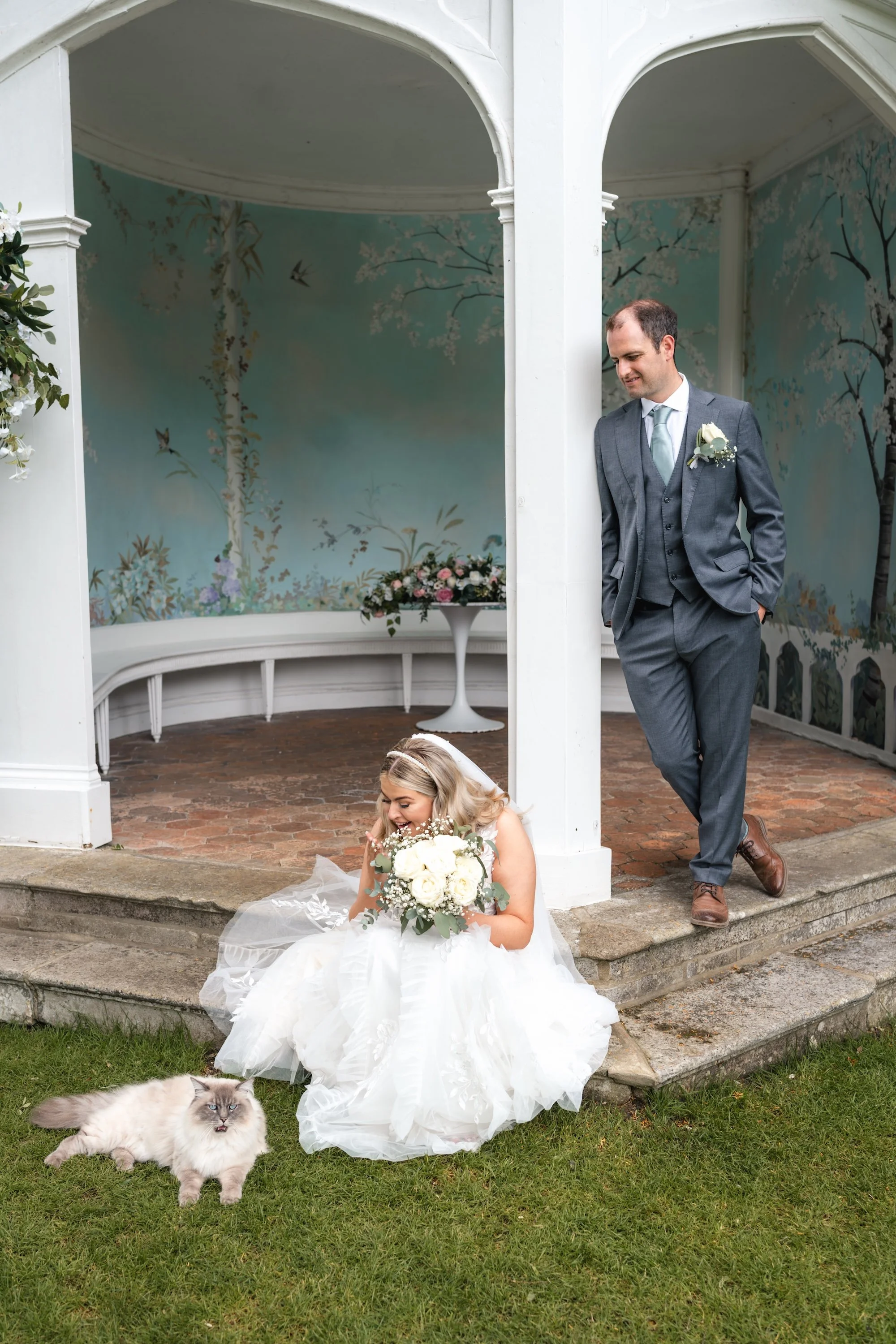 Bride stopping to pet the resident cat at Wasing Park beside the Victorian Summerhouse during her wedding portraits