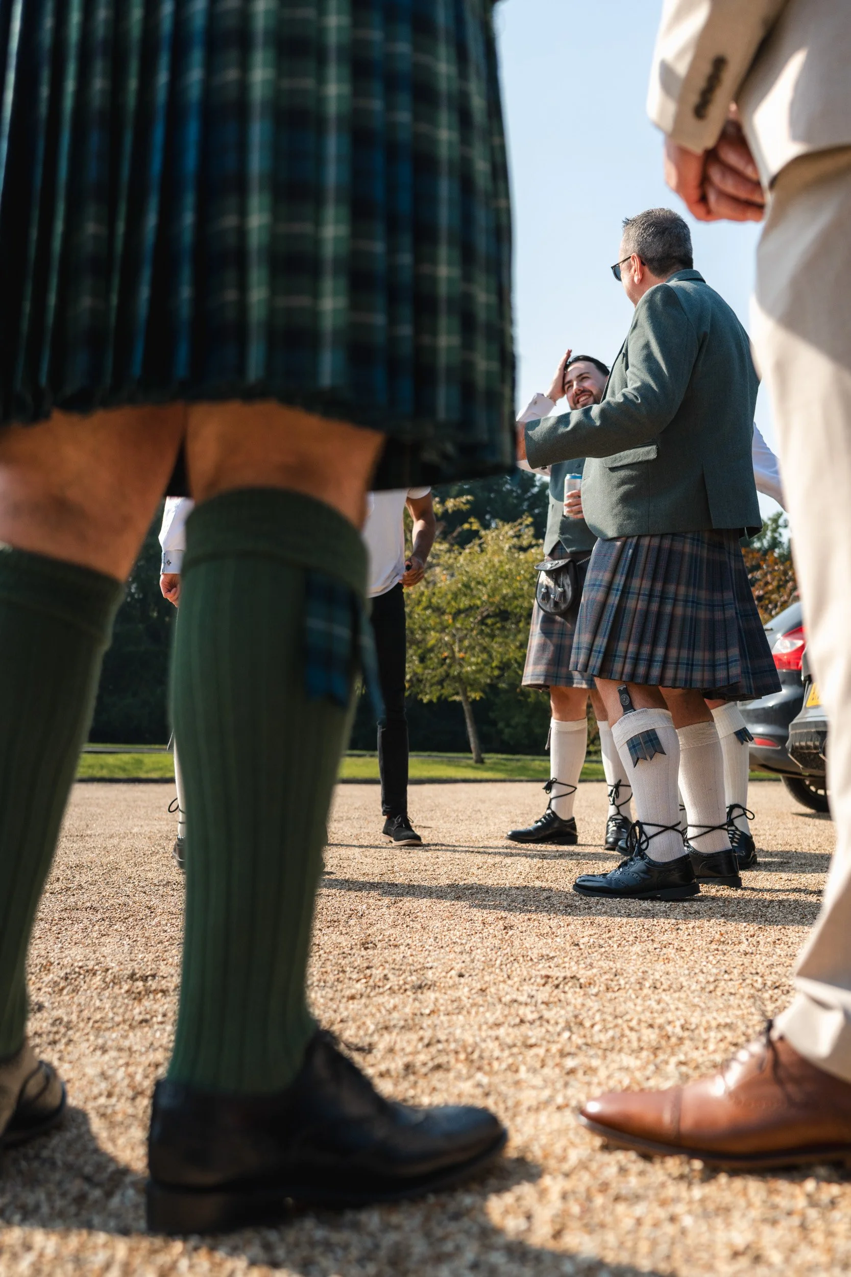 Guests wearing traditional kilts gathering outside during Rivervale Barn wedding drinks reception in Hampshire