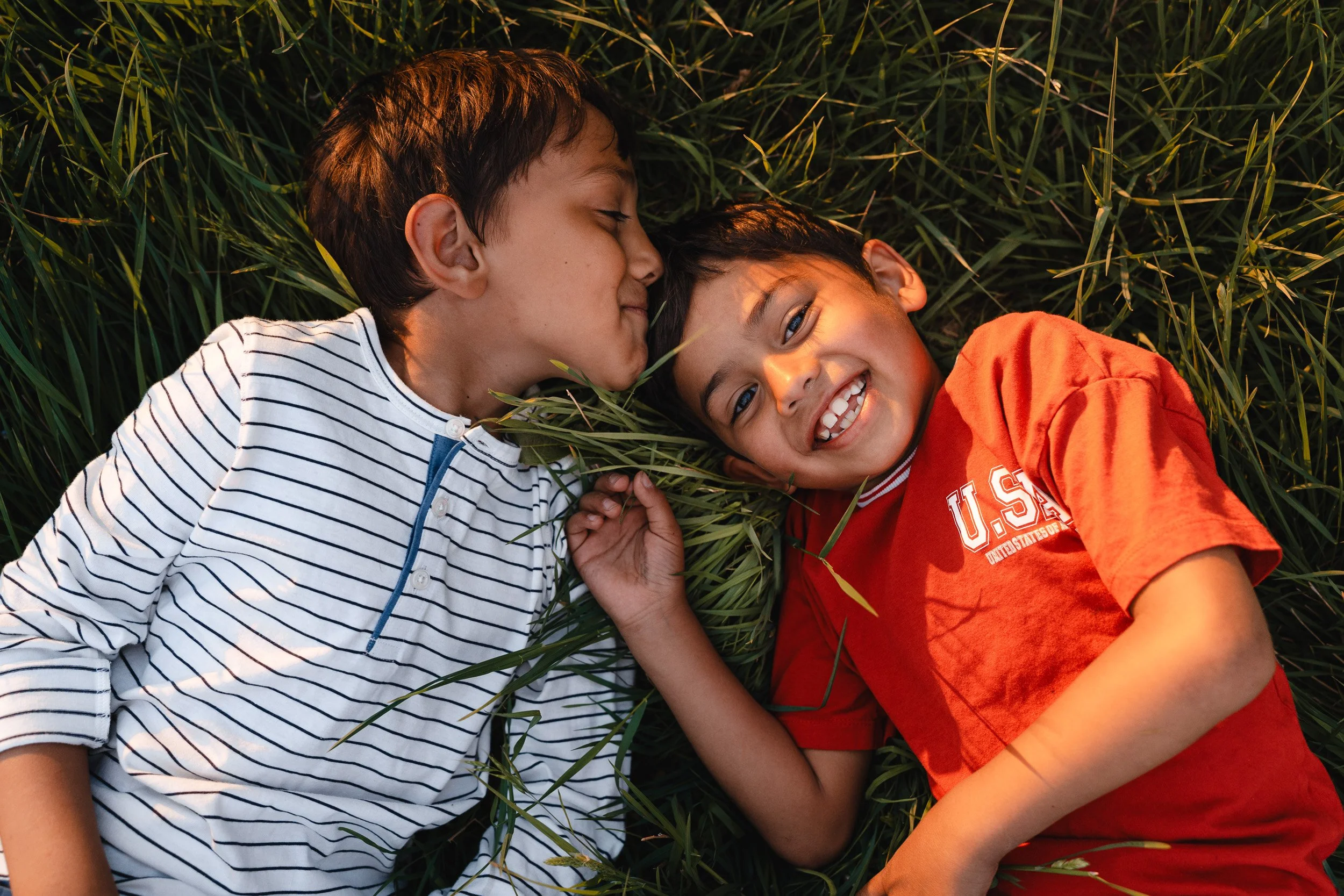 Two young brothers lying in the long grass at golden hour during a relaxed outdoor family photography session in Amersham, Buckinghamshire 
