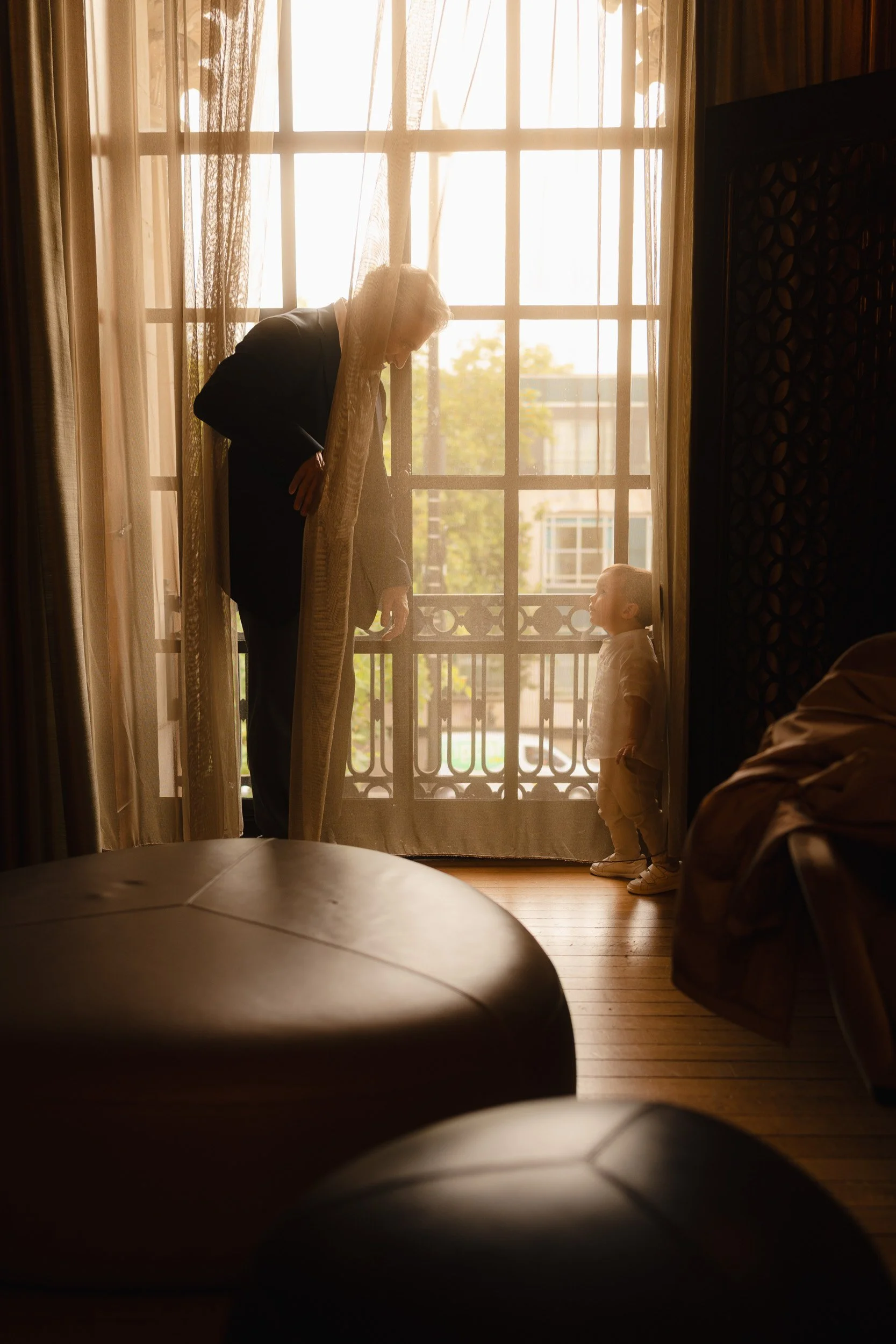 Father of the bride gazes down at his grandson in  golden window light  at Marylebone Town Hall Registry Office in London 