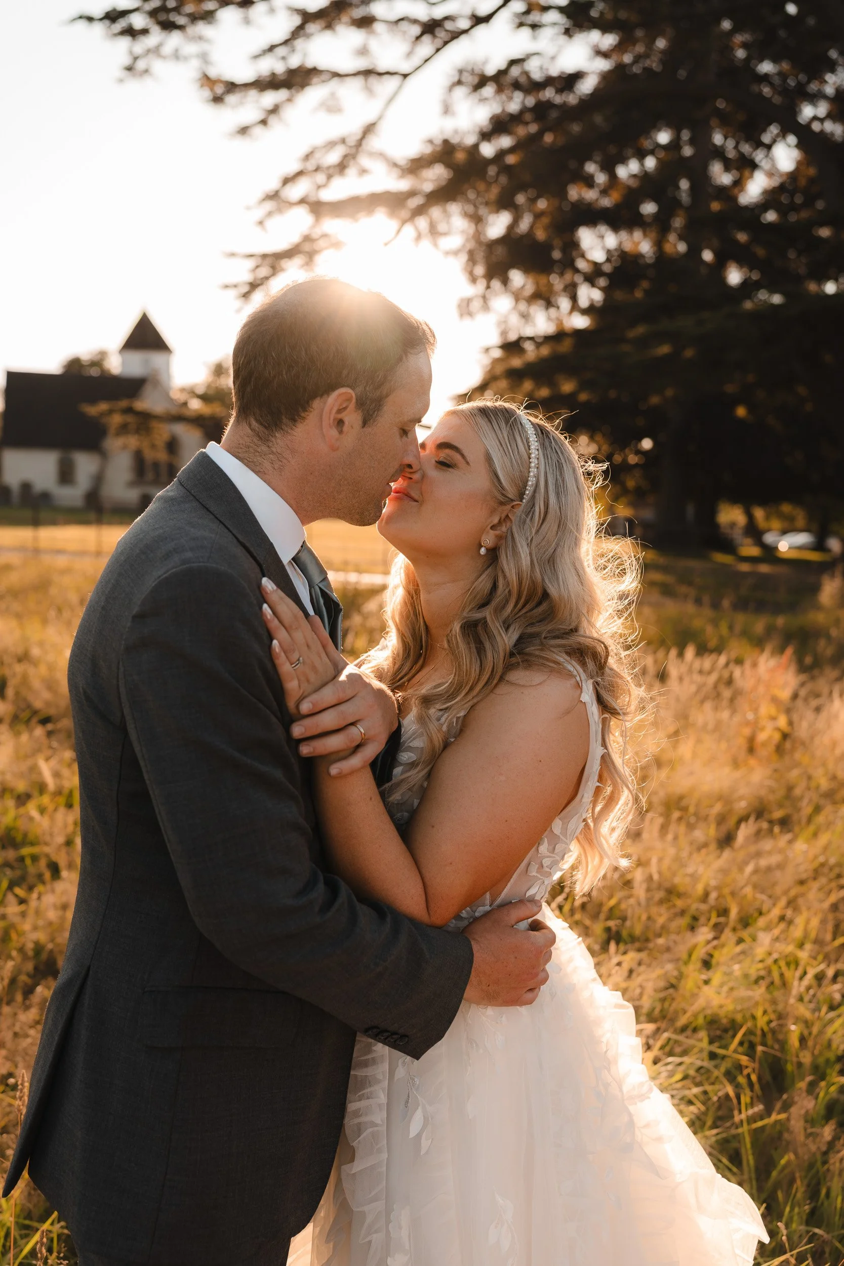 Bride and groom kissing in the golden sunset light in the meadows of Wasing Park in Berkshire