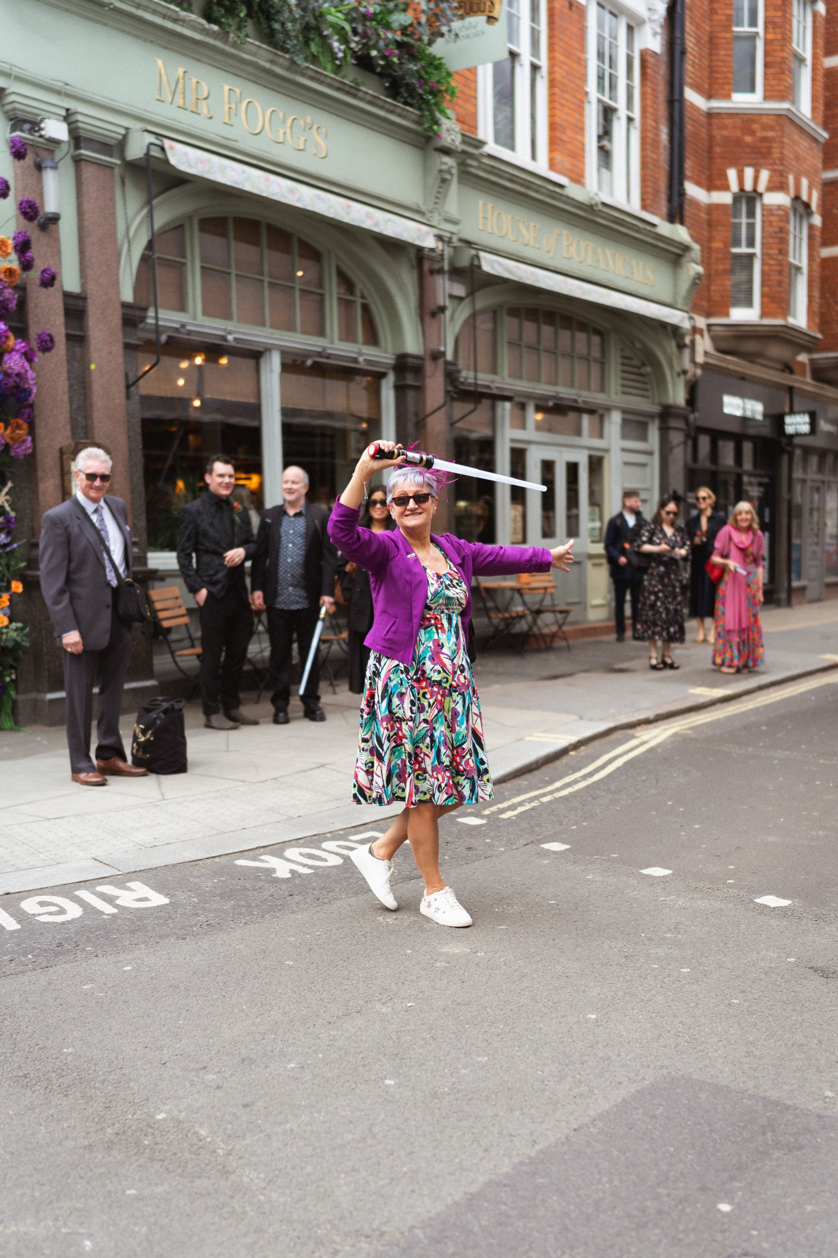 Wedding guest waving a lightsaber to guide guests toward the reception at the Union Club in Soho, London
