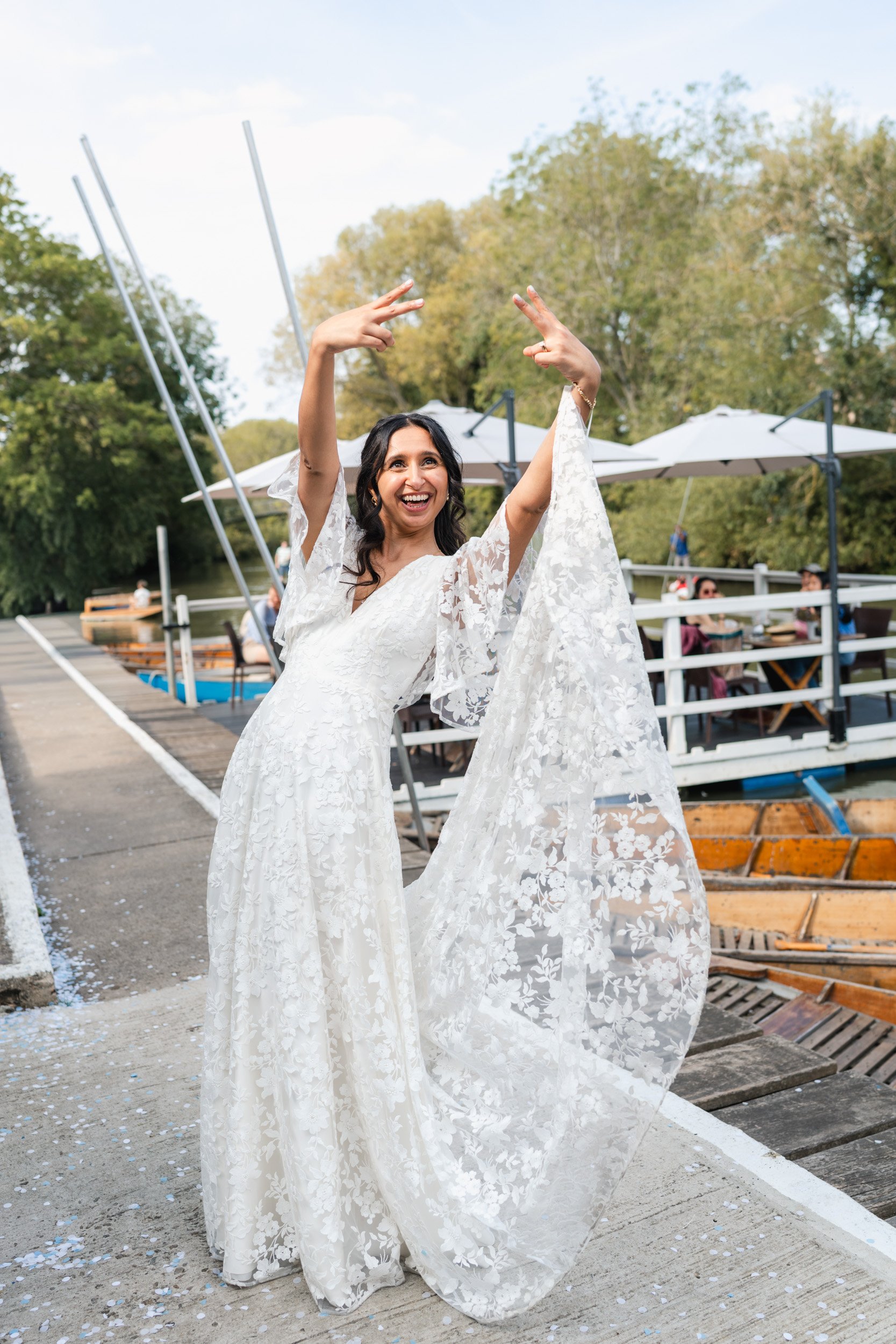 Bride laughing and playfully flipping the bird to cheering guests outside Cherwell Boathouse in Oxford 