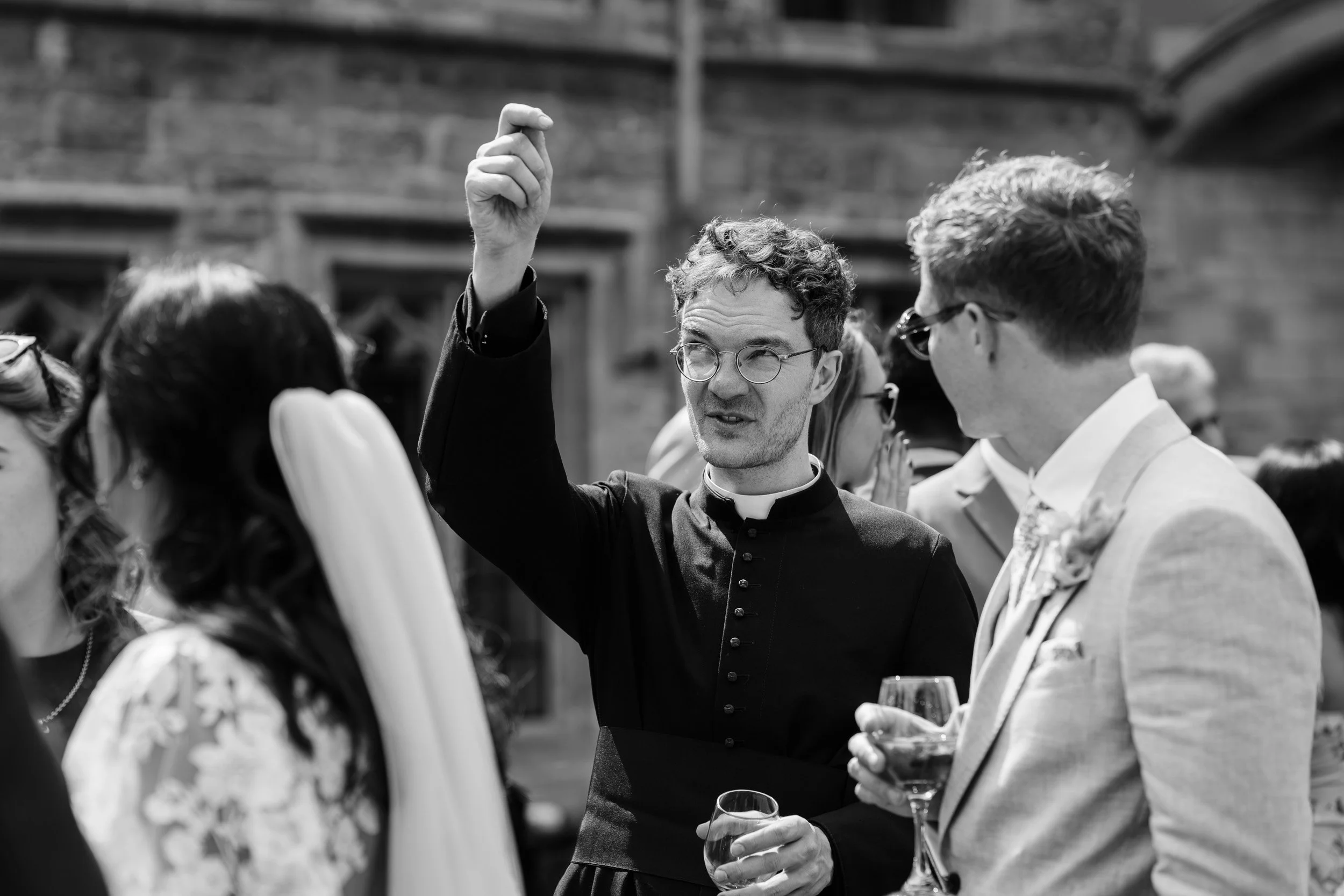 Church of England vicar chatting with wedding guests in a the garden of an Oxford University college for after wedding drinks in Oxford, England