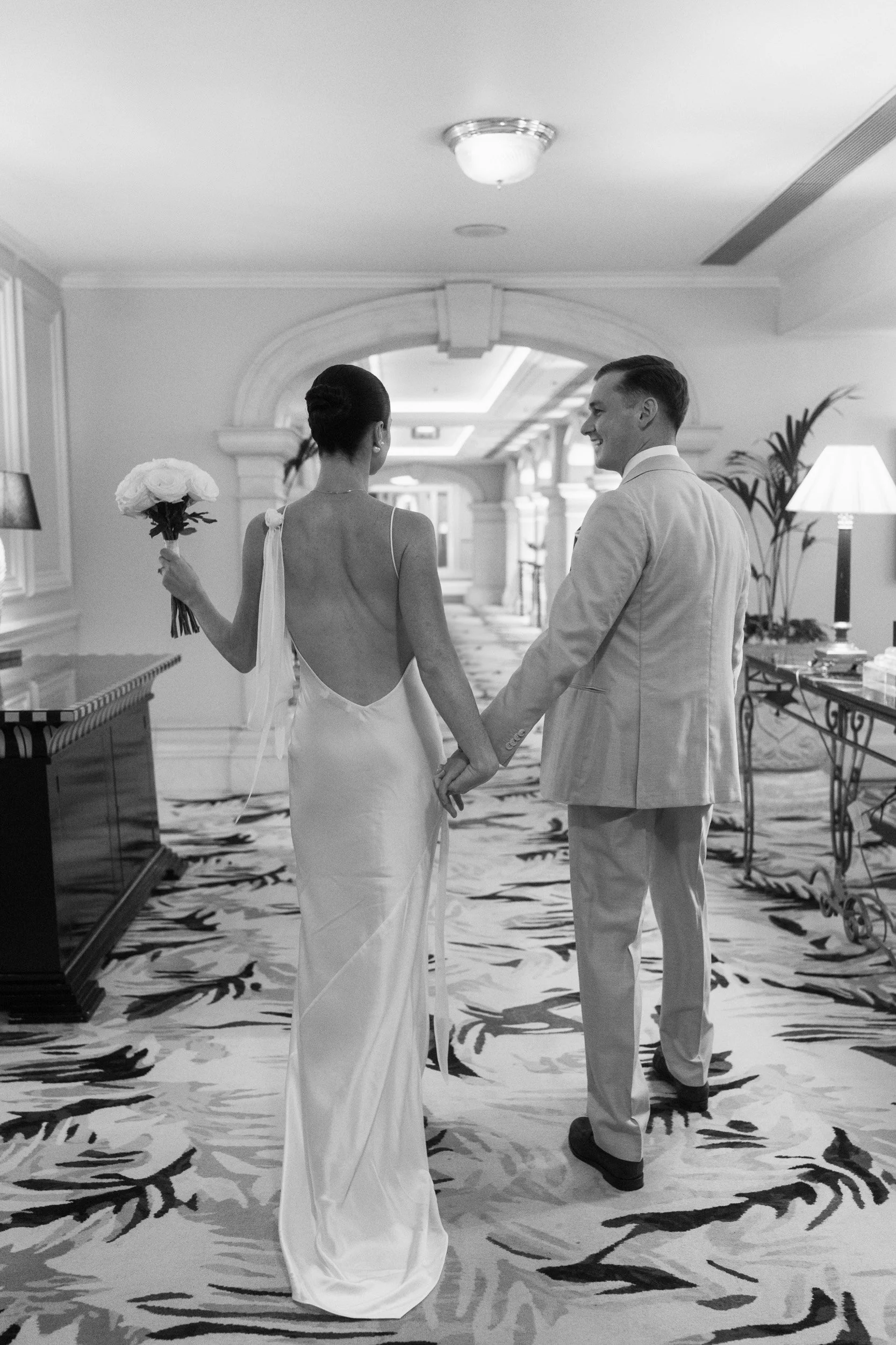 Bride and groom walking though The Landmark Hotel,  London in Marylebone holding her bouquet high