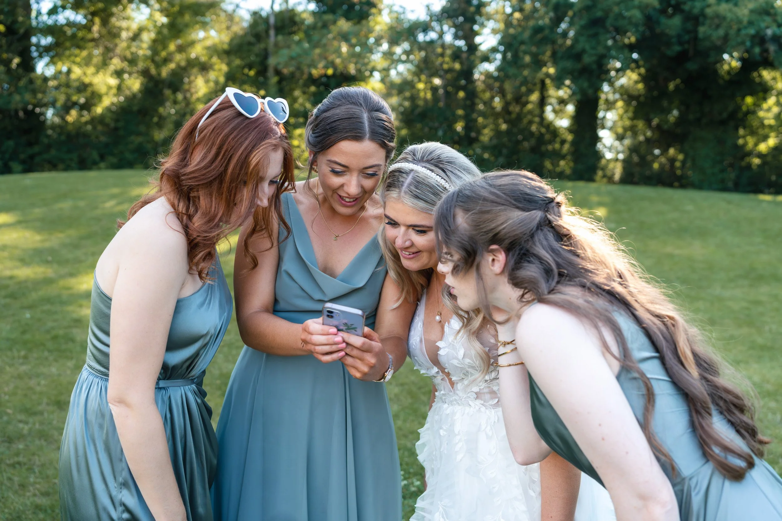 Bride and her bridesmaids giggling looking at photos taken on her iphone at the wedding reception at Wasing Park in Berkshire