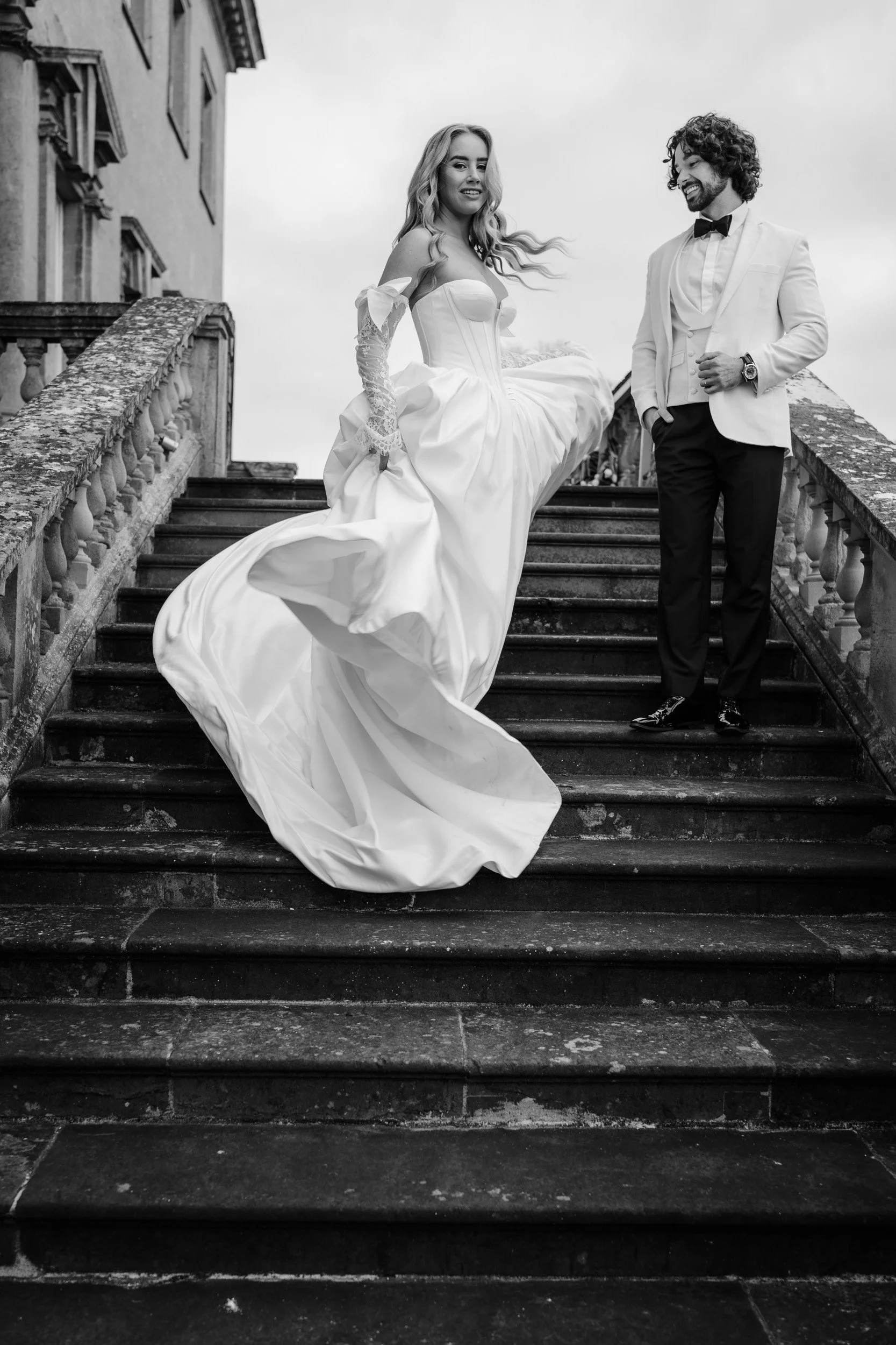 Bride and groom on the steps of Kirtlington Park in Oxfordshire with the wind catching the brides dress