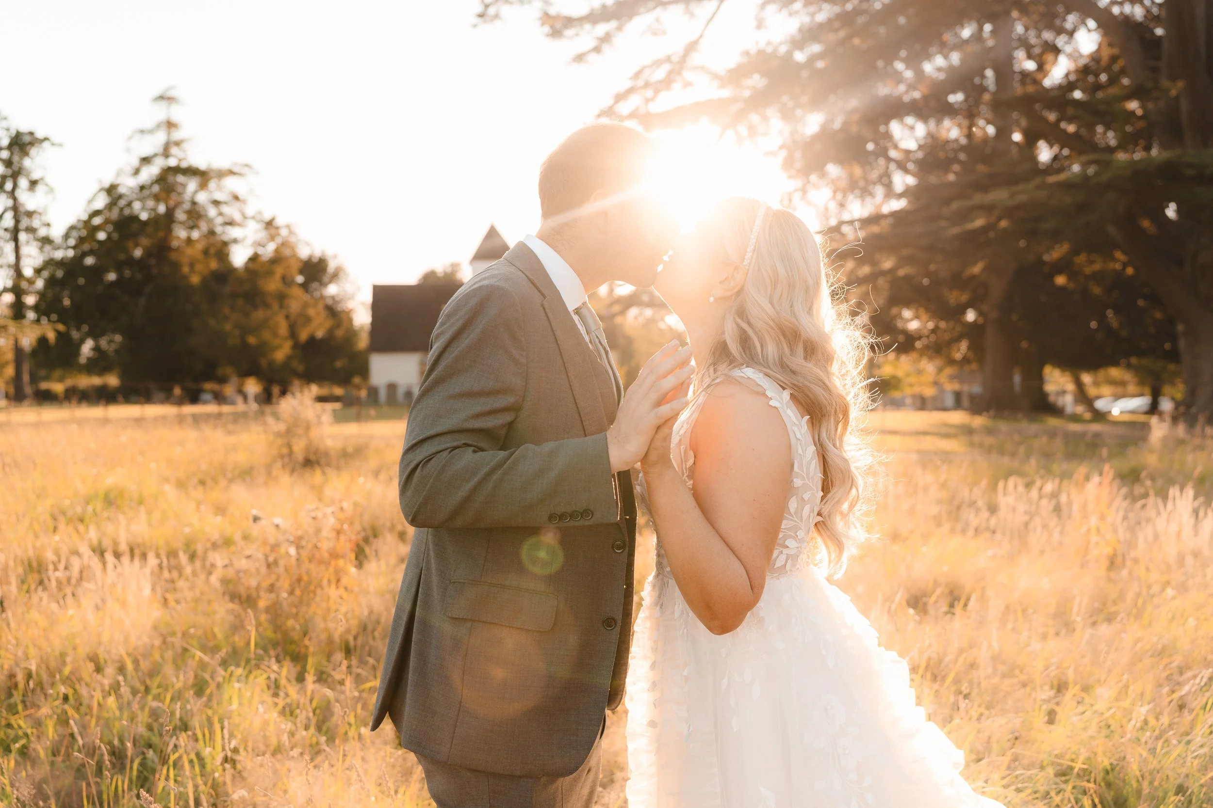 Bride and groom kissing in the golden sunset light in the meadows of Wasing Park in Berkshire