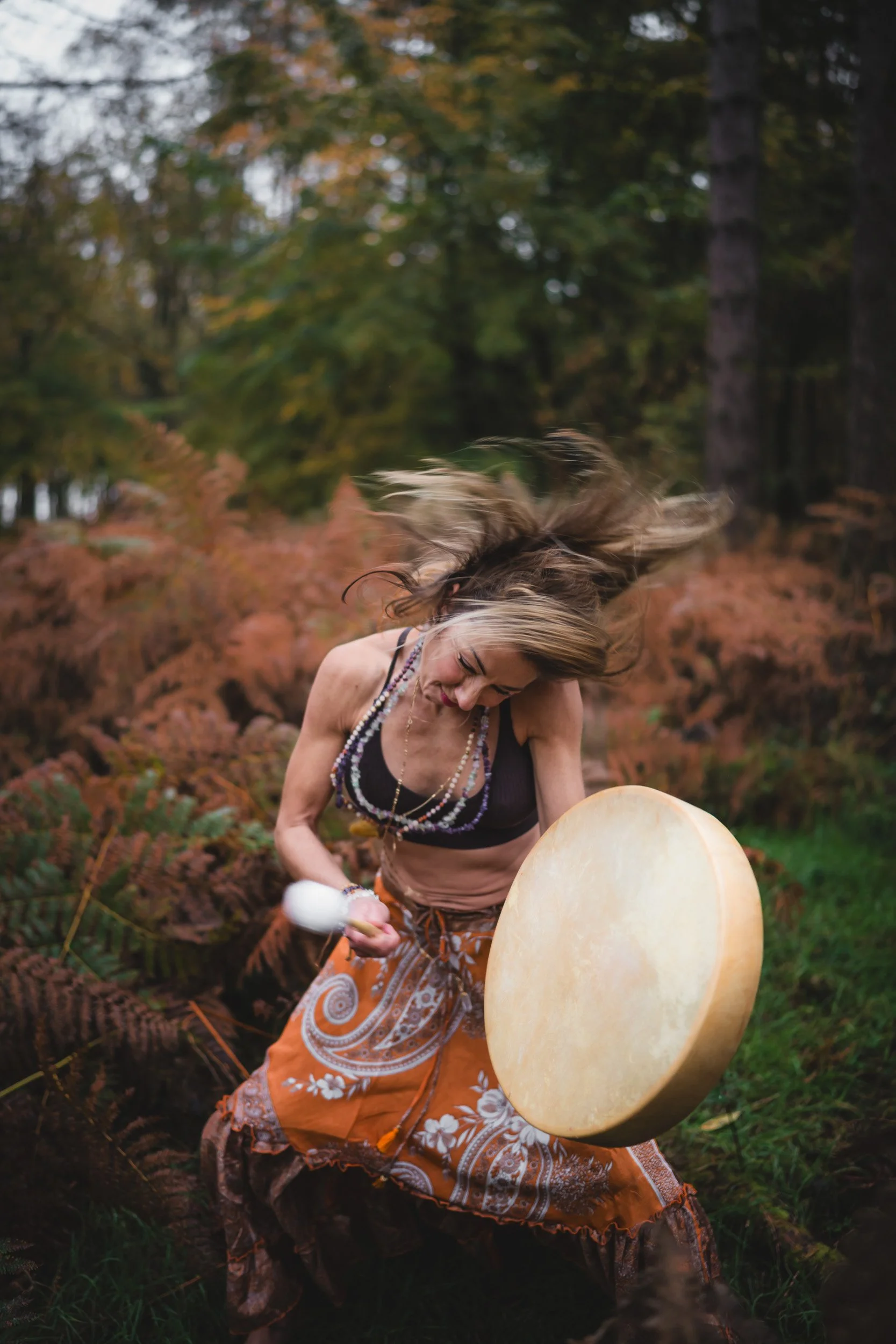 Sound healer playing a drum and dancing in the woodlands during a  personal branding shoot in Amersham Buckinghamshire