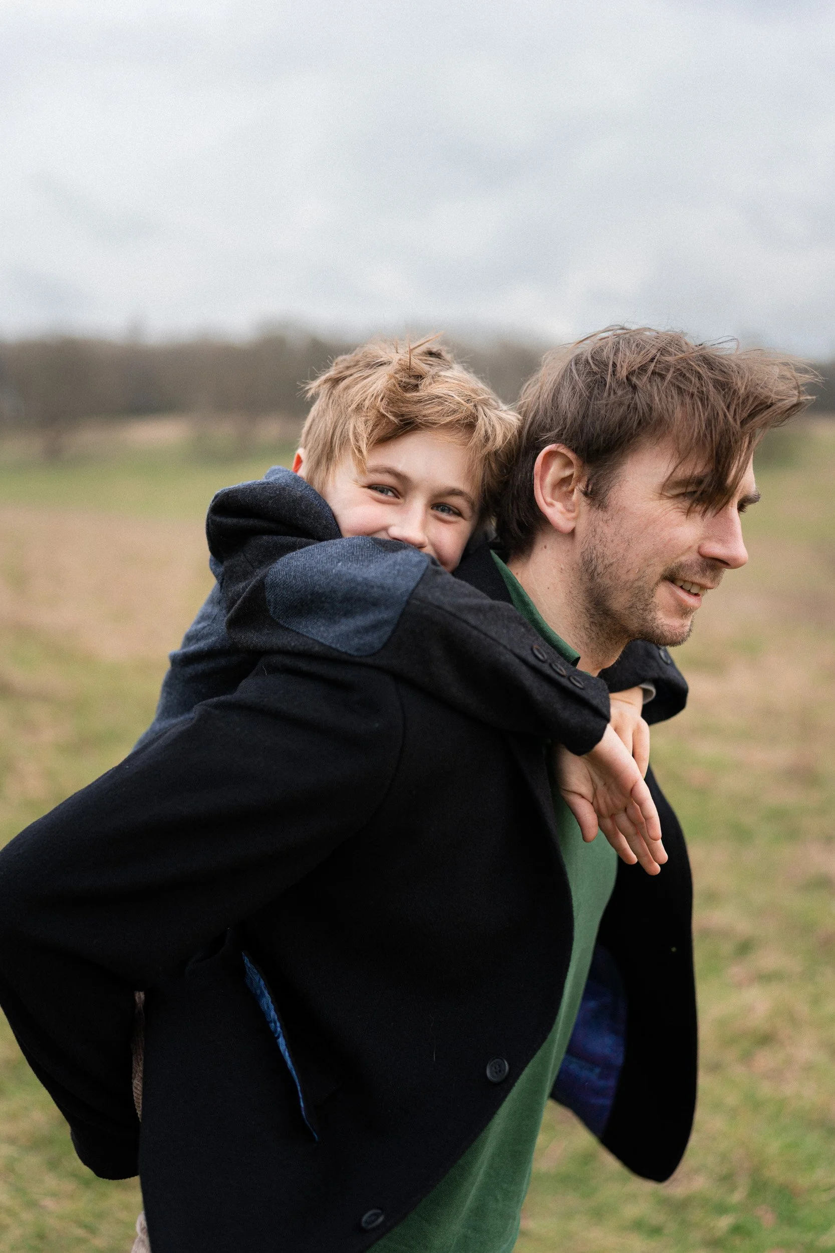 Little boy having a piggy back on a walk through the fields with his dad on a family portrait session in Great Missenden, Buckinghamshire