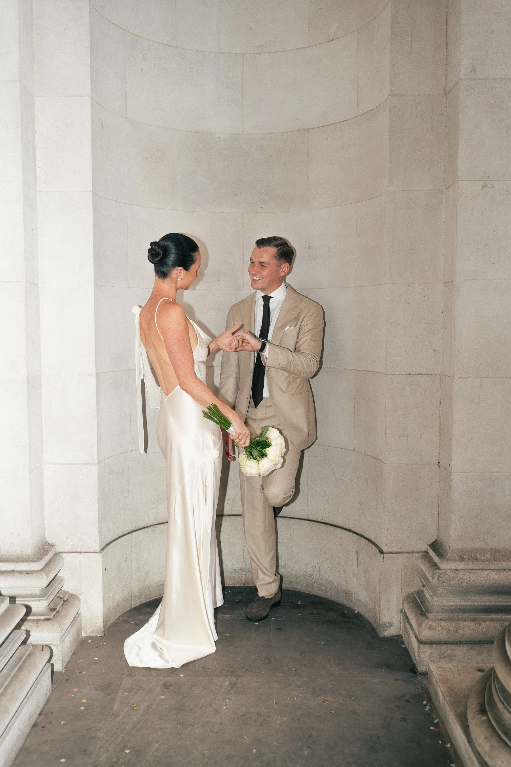 Bride and groom holding hands and smiling at each other outside Marylebone Registry Office in London