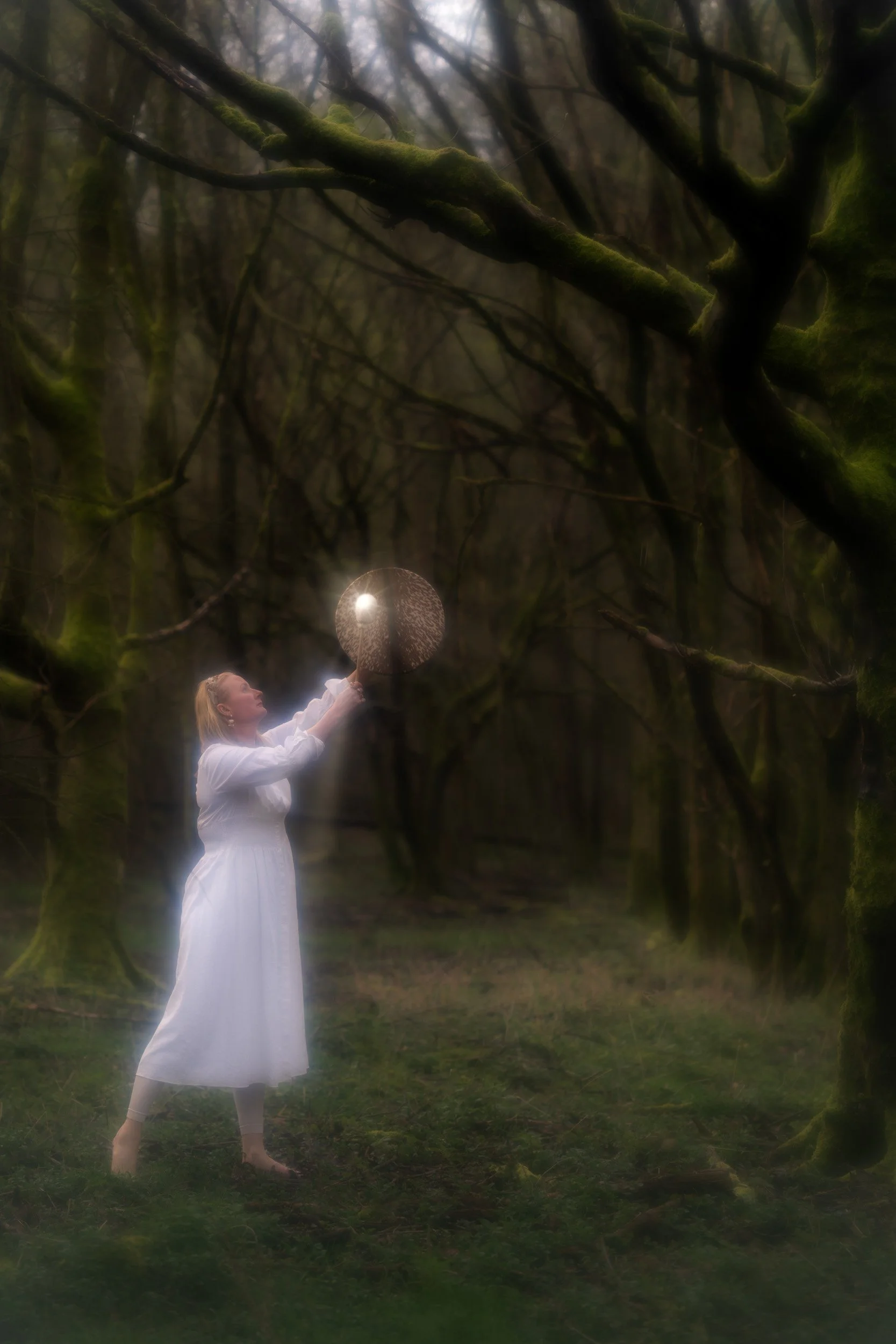 Sound healer beating a shamanic drum in the woodland during a sound healing session in Amersham Buckinghamshire