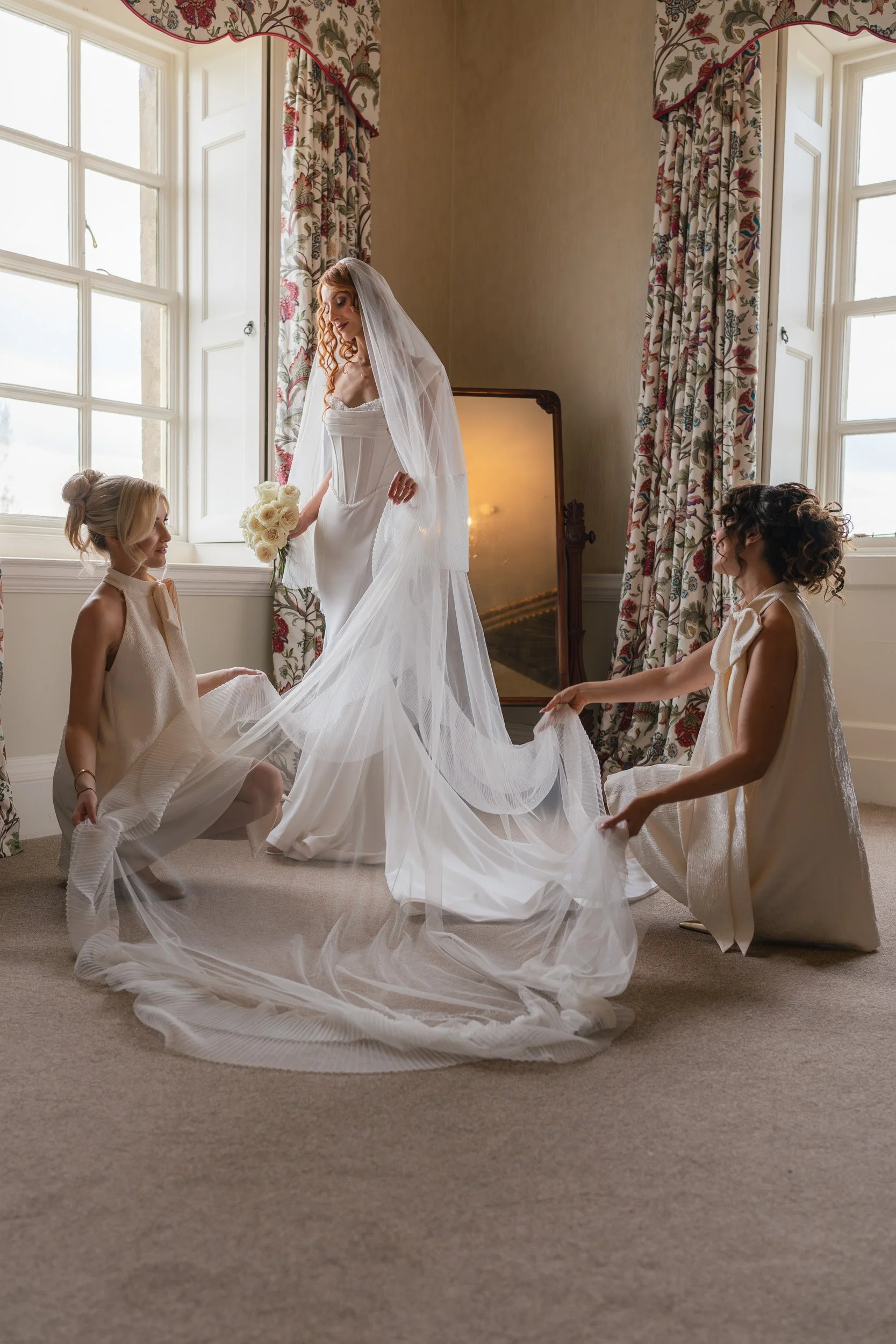 Bridesmaids helping the bride with her veil while getting ready  at Kirtlington Park in Oxfordshire