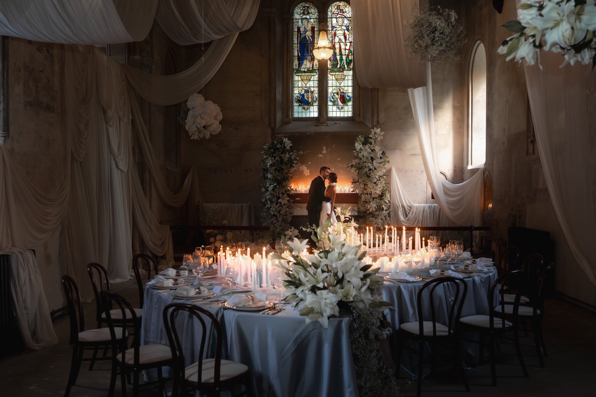 Bride and Groom sharing their first kiss inside The Bell Tower at The Elvetham surrounded by candlelight, flowers, silk drapes and stained glass