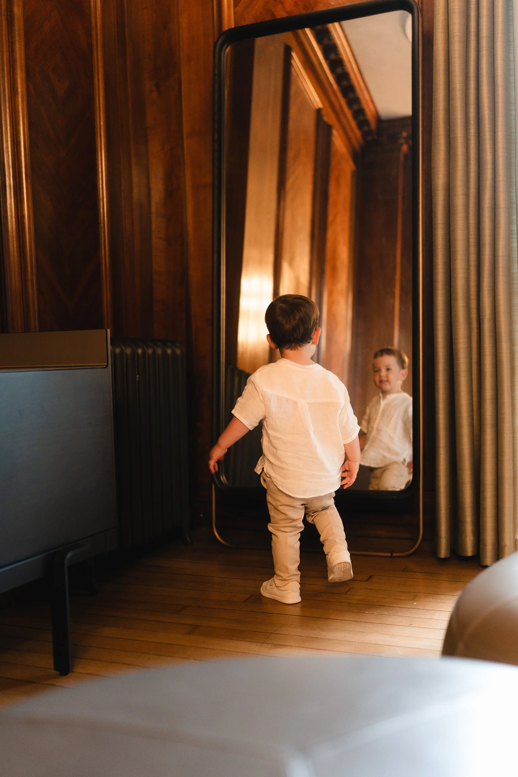 Bride and grooms son in  golden window light smiling at himself in the mirror at Marylebone Town Hall Registry Office in London 