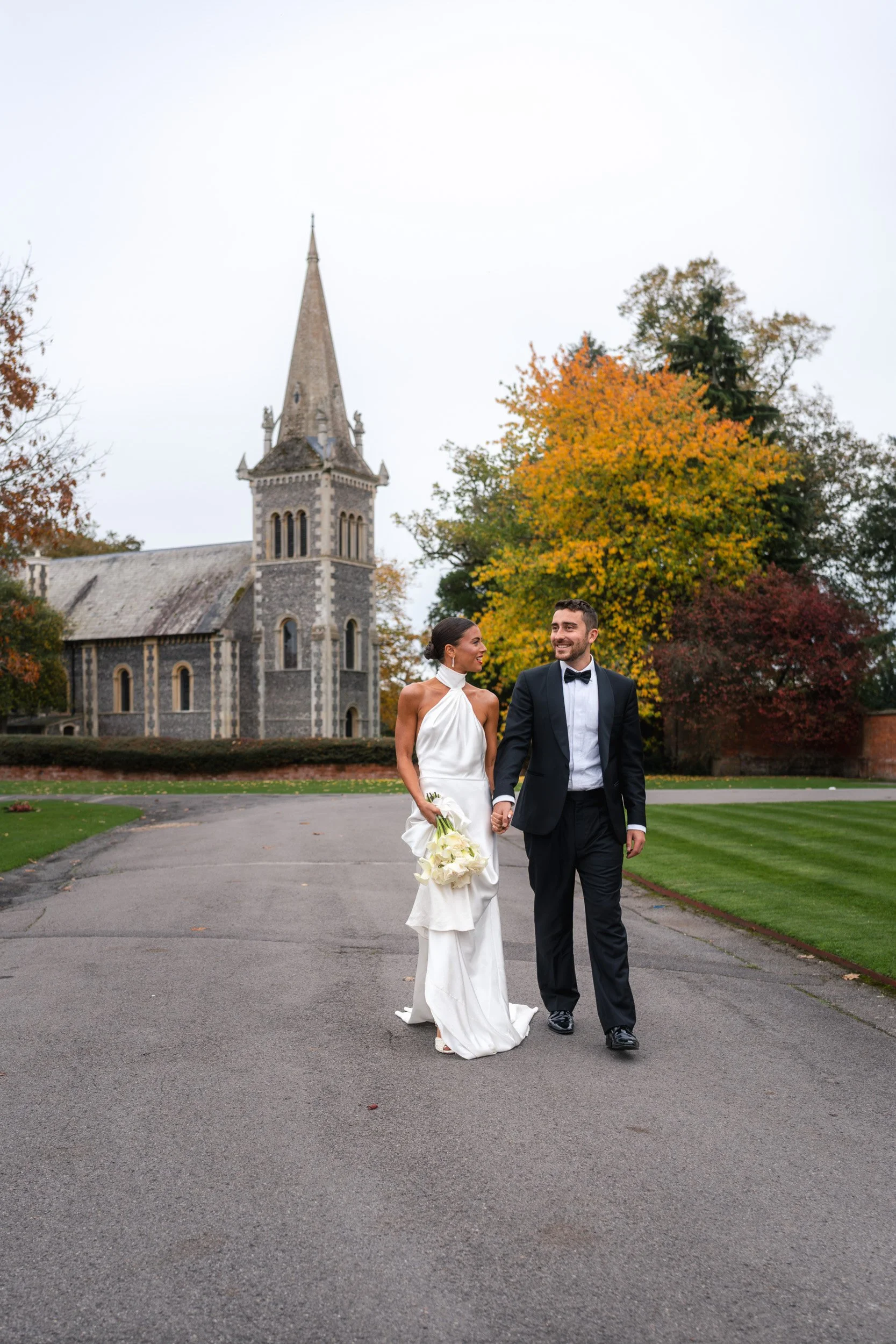 Bride and groom walking hand in hand in front of The Bell Tower at The Elvetham Hotel in Hampshire