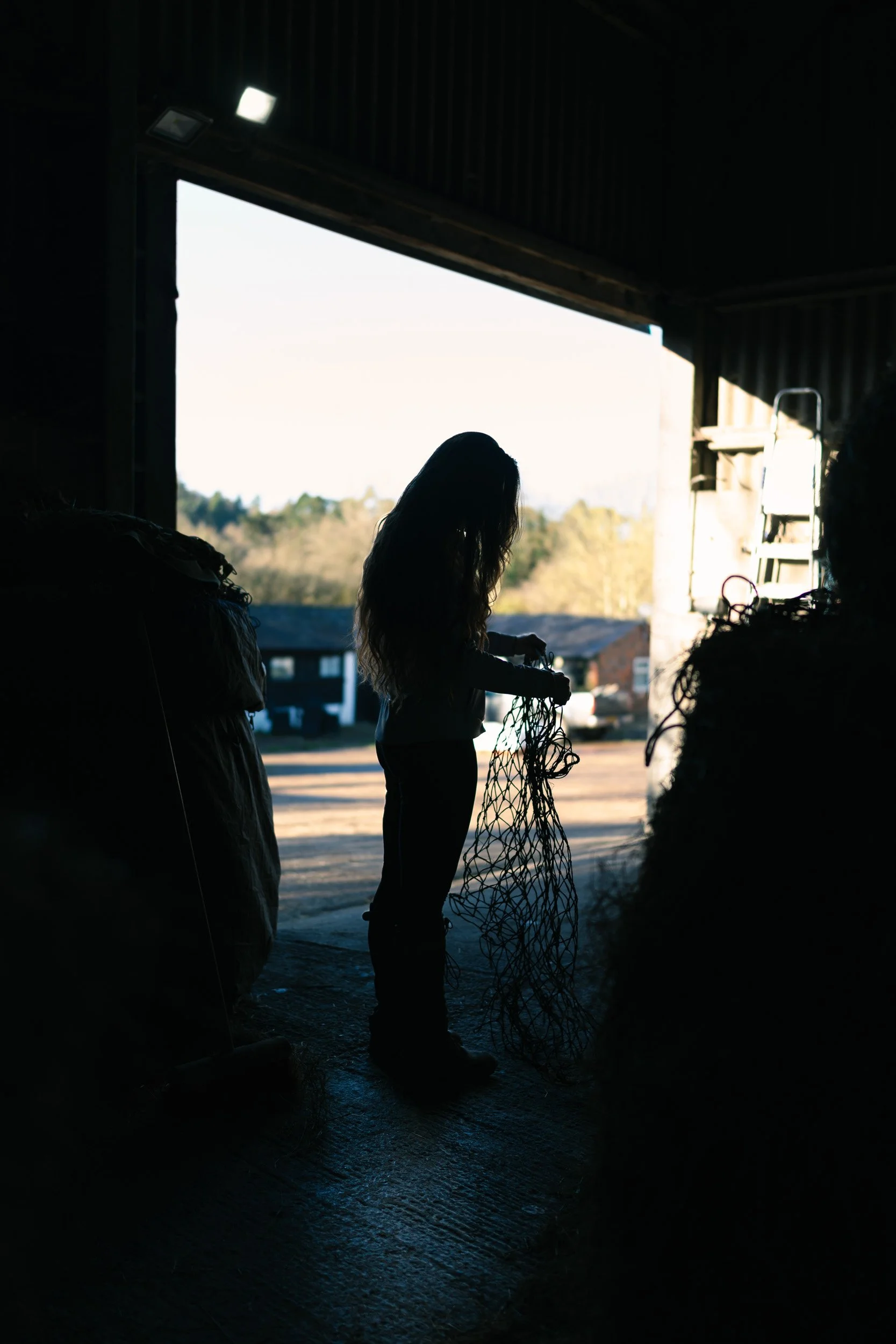 Silhouette of an Equestrian fitness coach filling hay bales in the stable door way at Sean Hardy Horse Training in Great Missenden Buckinghamshire during a branding session