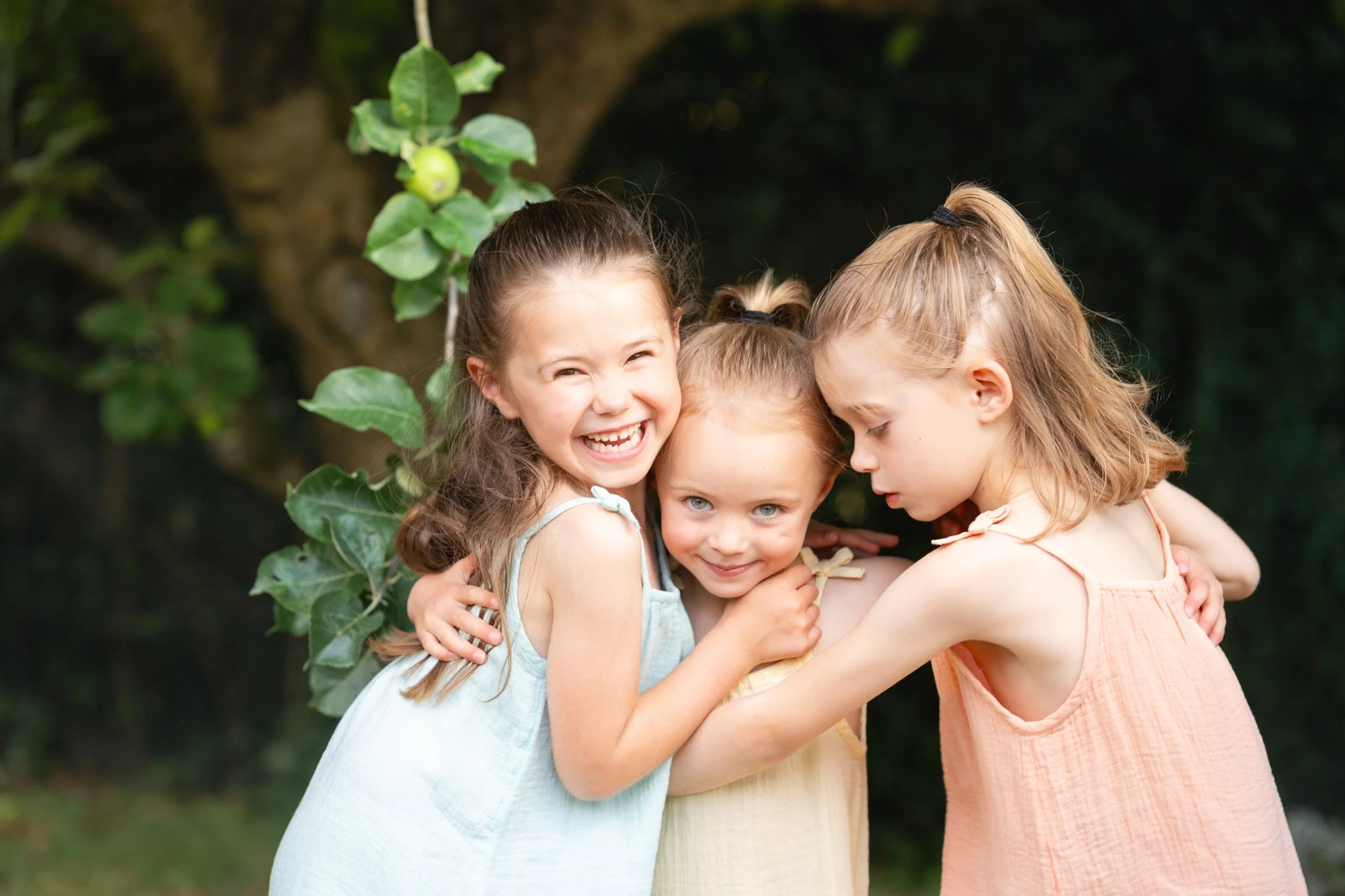 Three young sisters hugging under the apple tree during a natural summer family photoshoot  in Amersham, Buckinghamshire