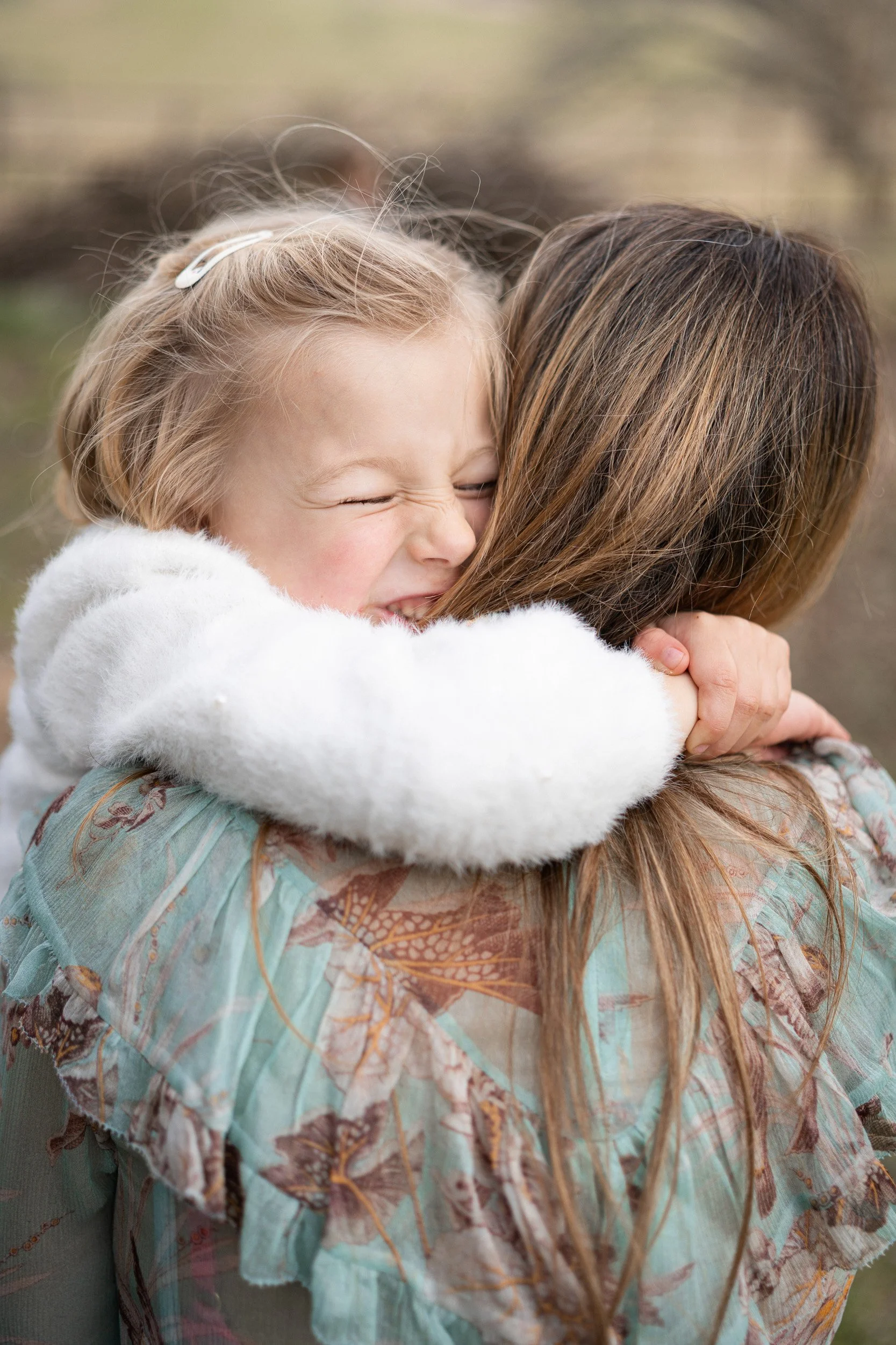 Little girl smiling snuggling into her mothers neck in the golden light  on a family photoshoot in Great Missenden, Buckinghamshire