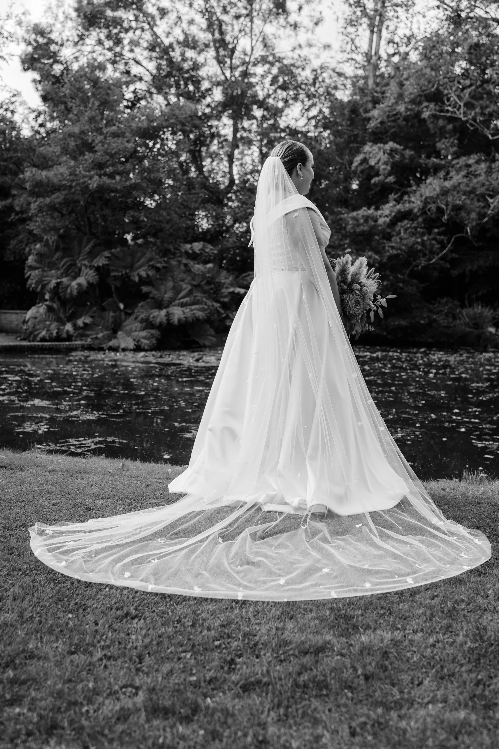 Bride in her vale over looking the pond in the gardens of Rivervale Barn wedding venue in Hampshire