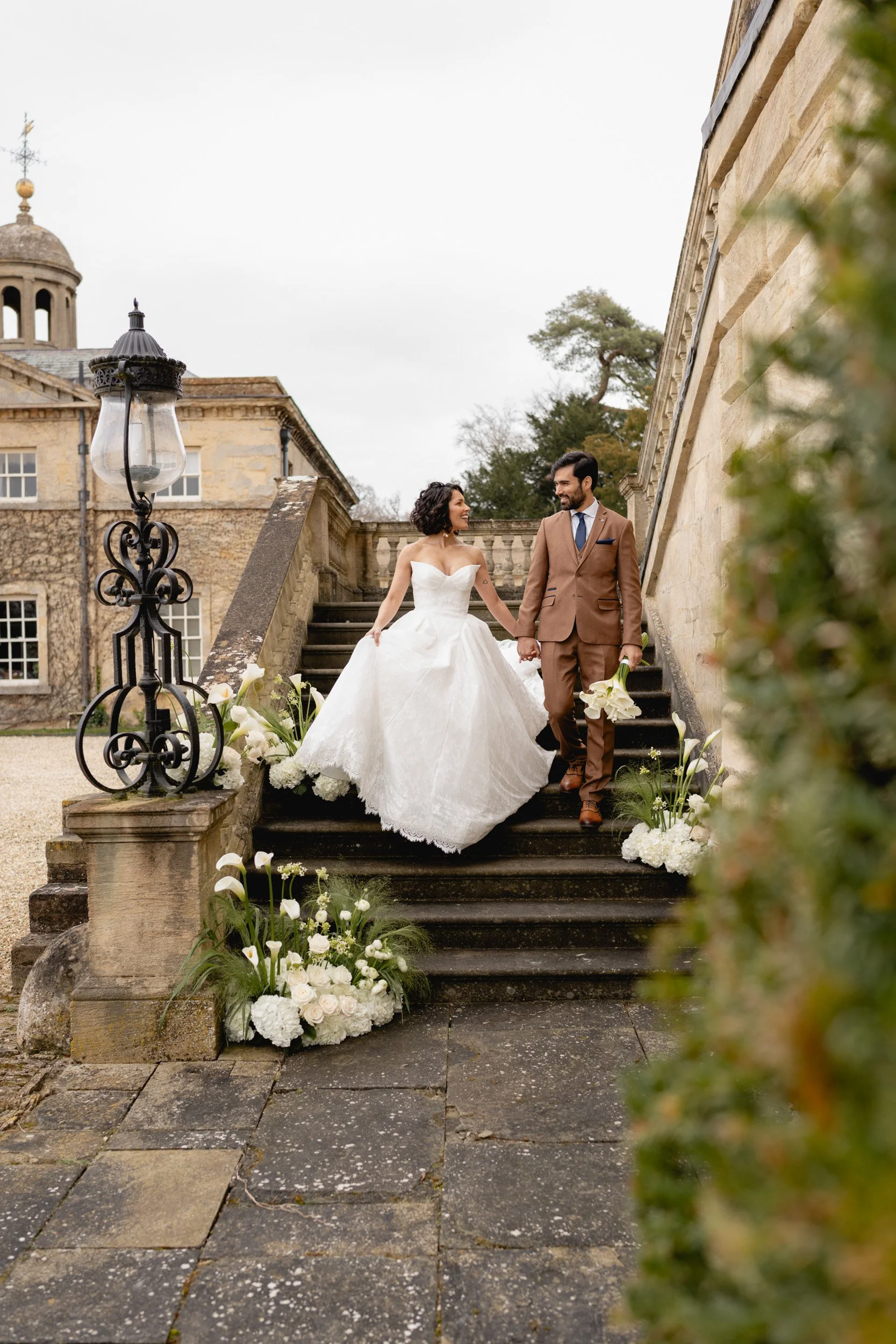 Bride and groom walking down the flower lined stairs outside Kirtlington Park in Oxfordshire