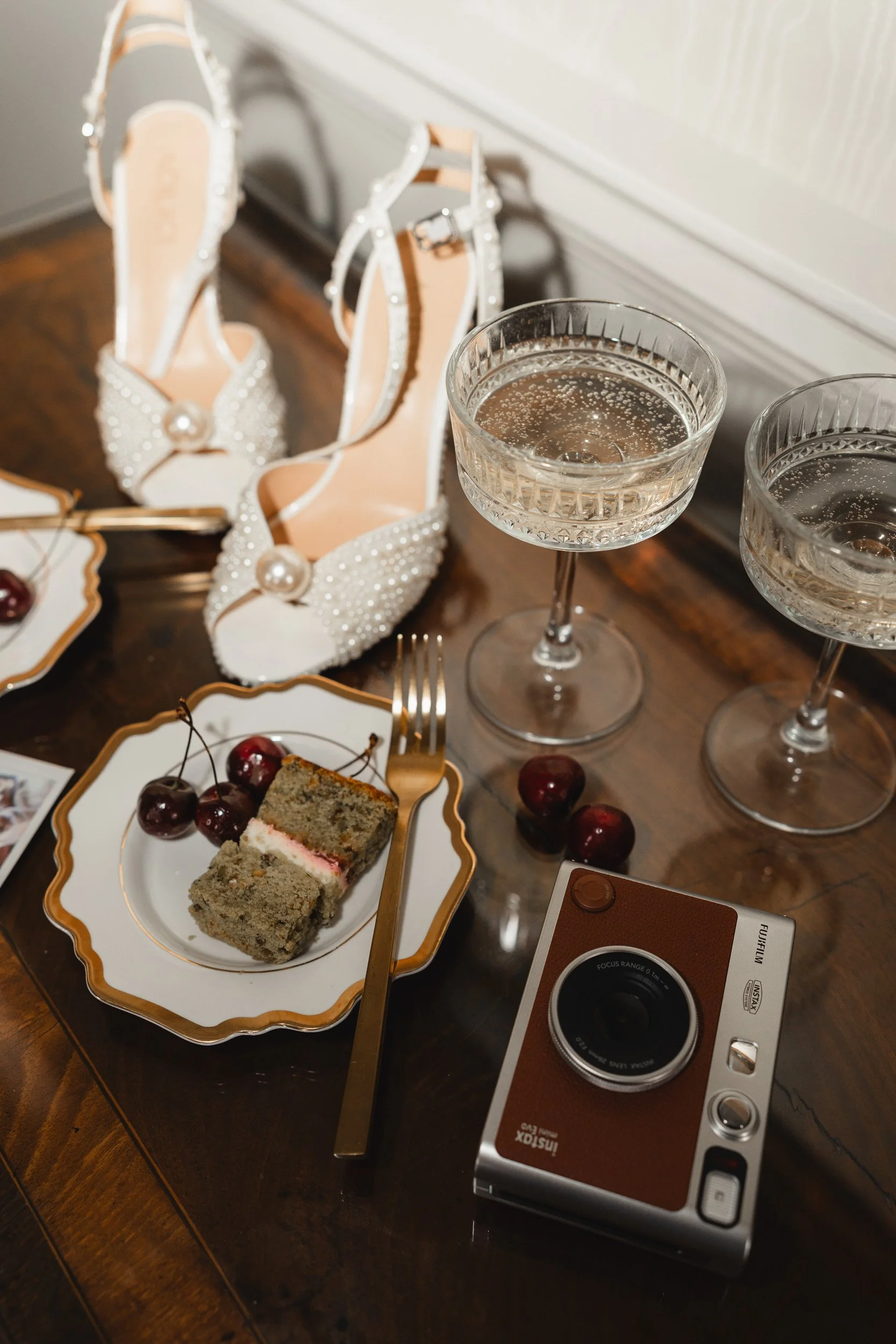 Wedding details including bridal shoes, champagne glasses, cake and instant camera in a suite at Kirtlington Park in Oxfordshire
